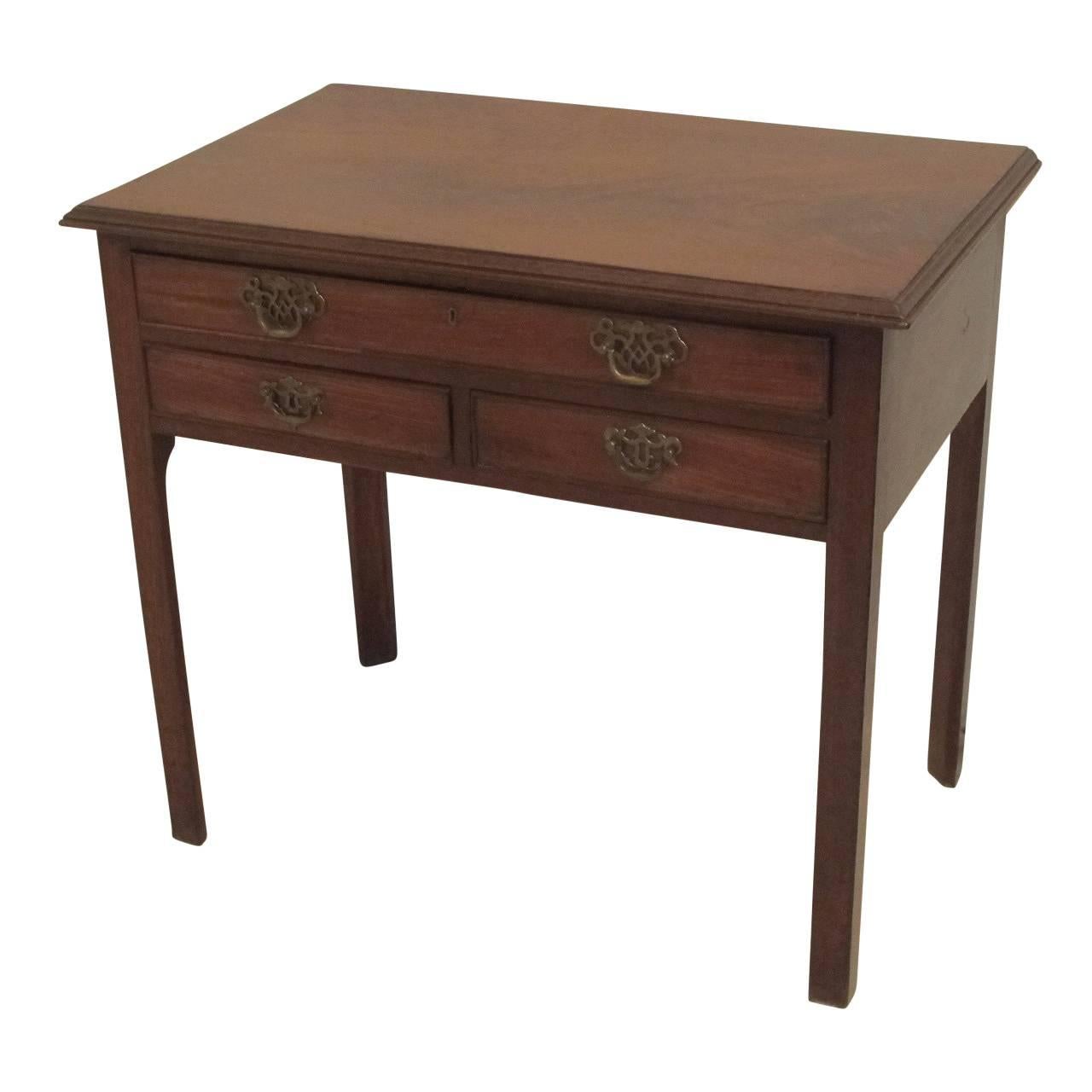 Three-drawer mahogany side table having a single long drawer over two short drawers standing on square legs with canted inside, England, circa 1820.
