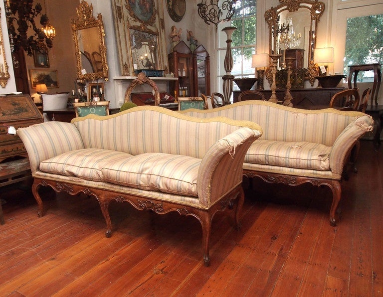 A pair of Italian Rococo settees, finely carved, and each having an arched, upholstered back with deeply canted arms. Loose, down filled cushions rest over an exposed, carved wood frame with a scalloped seat rail over S-curved legs. Presented as