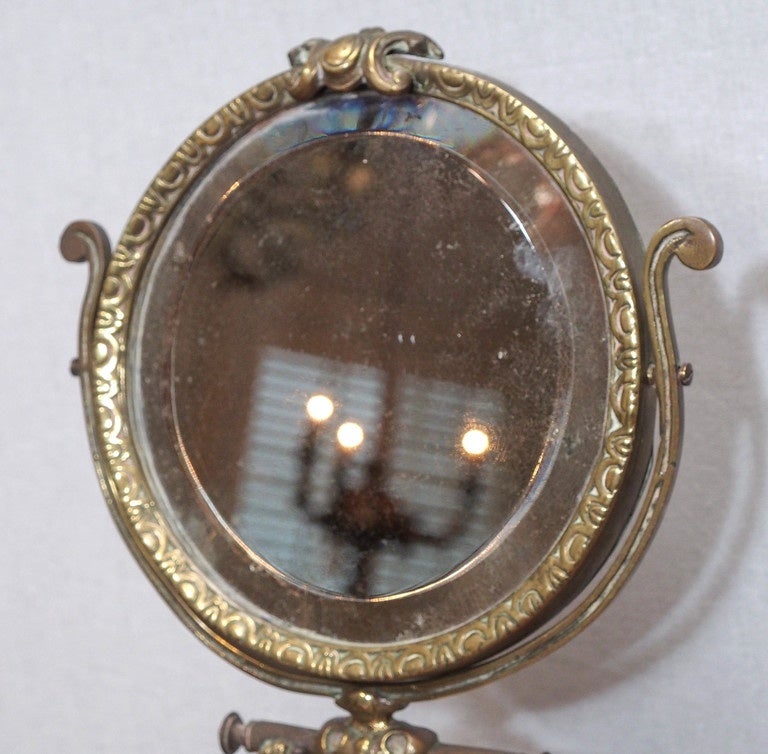 A bronze table mirror, the round, beveled glass set in an egg and dart frame supported by a caryatid with outstretched arms and the figure on a marble base.