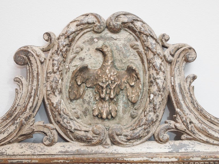 A large, Louis XVI style mirror, the frame with garland and scroll ornamentation and topped with a carved pediment sporting a dove.  Originally gilded, the frame now has a well worn painted finish, with traces of the gilding showing.