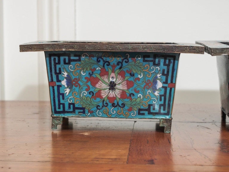 A pair of colorful, rectangular cloisonné planters with an overhanging rim and on stepped feet.