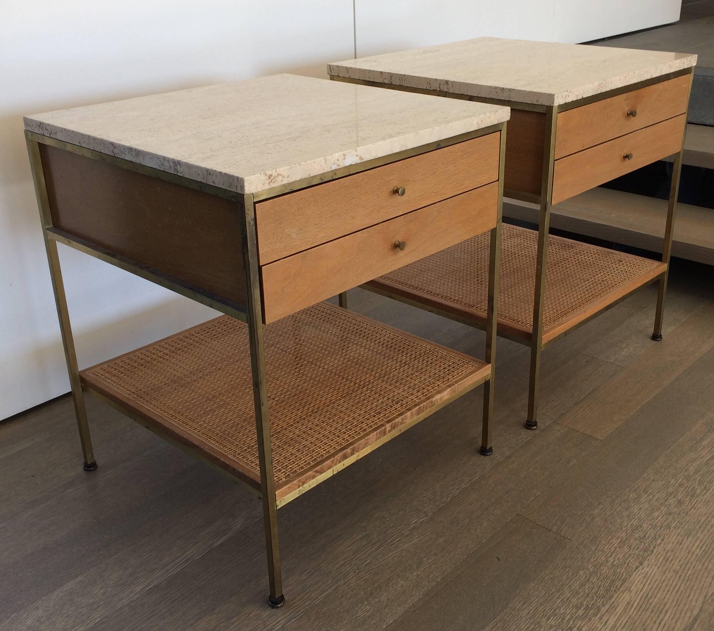 Pair of brass, blond mahogany two-drawer nightstands with travertine tops and lower caned shelf; designed by Paul McCobb for Calvin, retaining original maker tags. Great example of iconic Mid-Century design and materials.