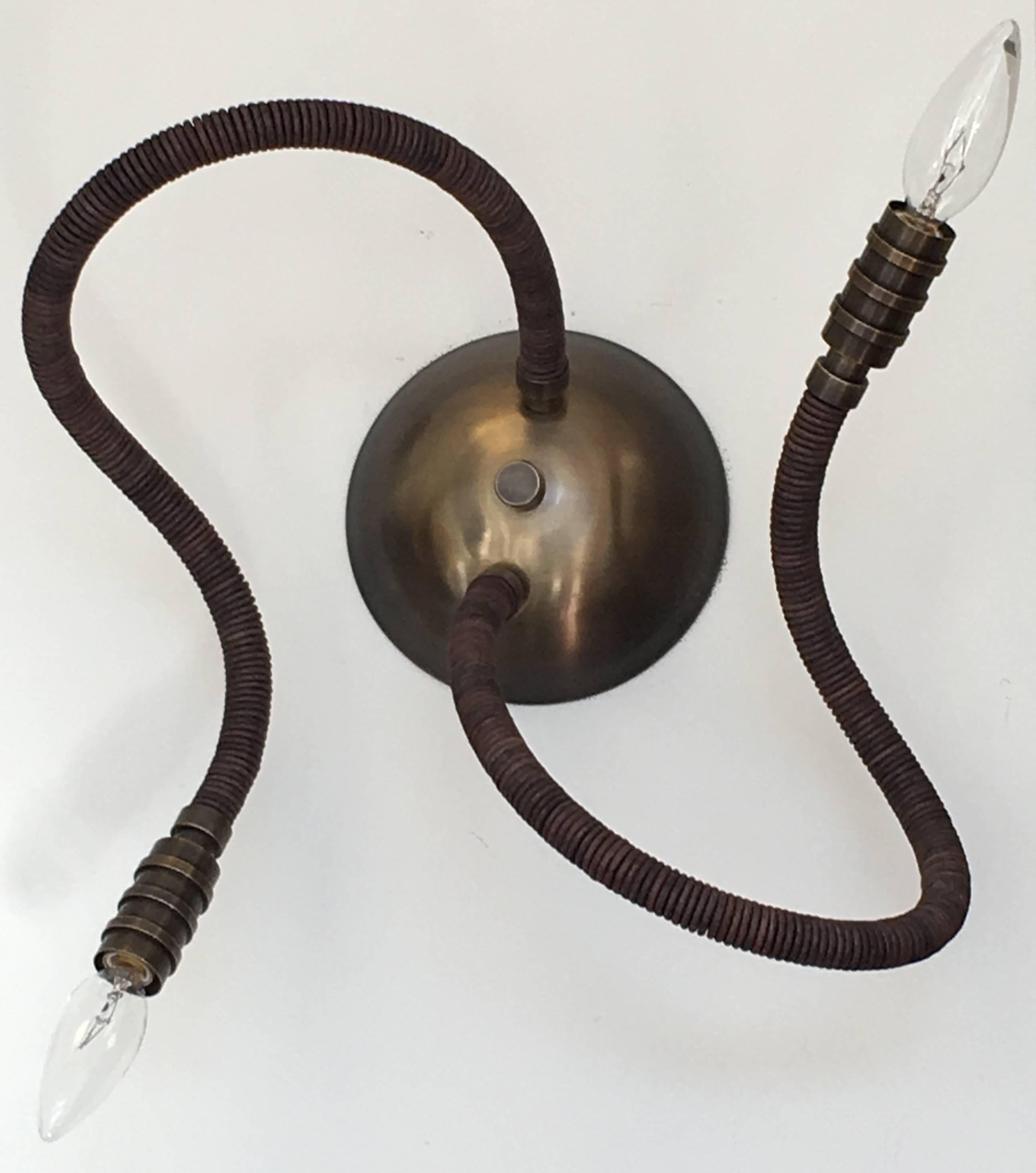 Adjustable leather 2 arm wall sconce which allow for playful poses and custom options; shown in natural brown bark leather. Artisanal luxe lighting, also available in a seven-arm chandelier. 30 leather colors; Brass (natural or oil rubbed) or