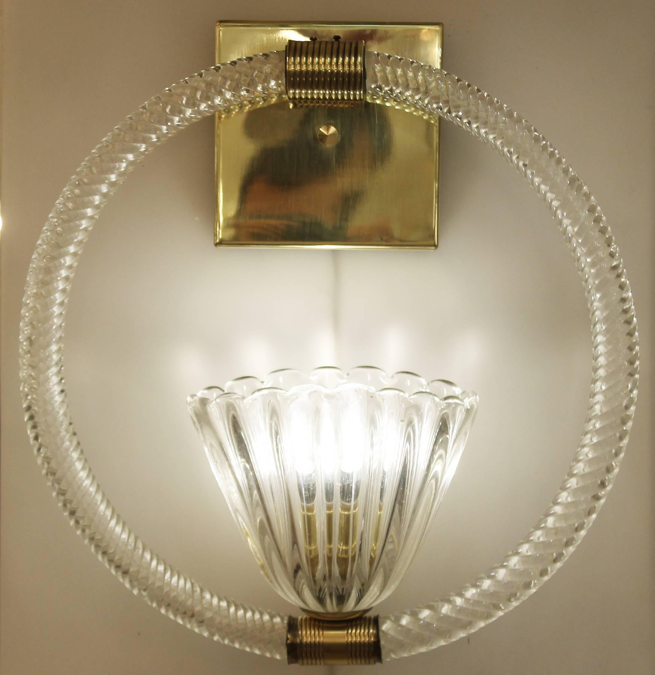Each sconce is composed of a glass shade connected to the backplate by a glass loop. The glass is clear and textured while the backplate and junctions are brass. The flower shaped shade holds one regular E27 socket. Backplate can be tilted to use as