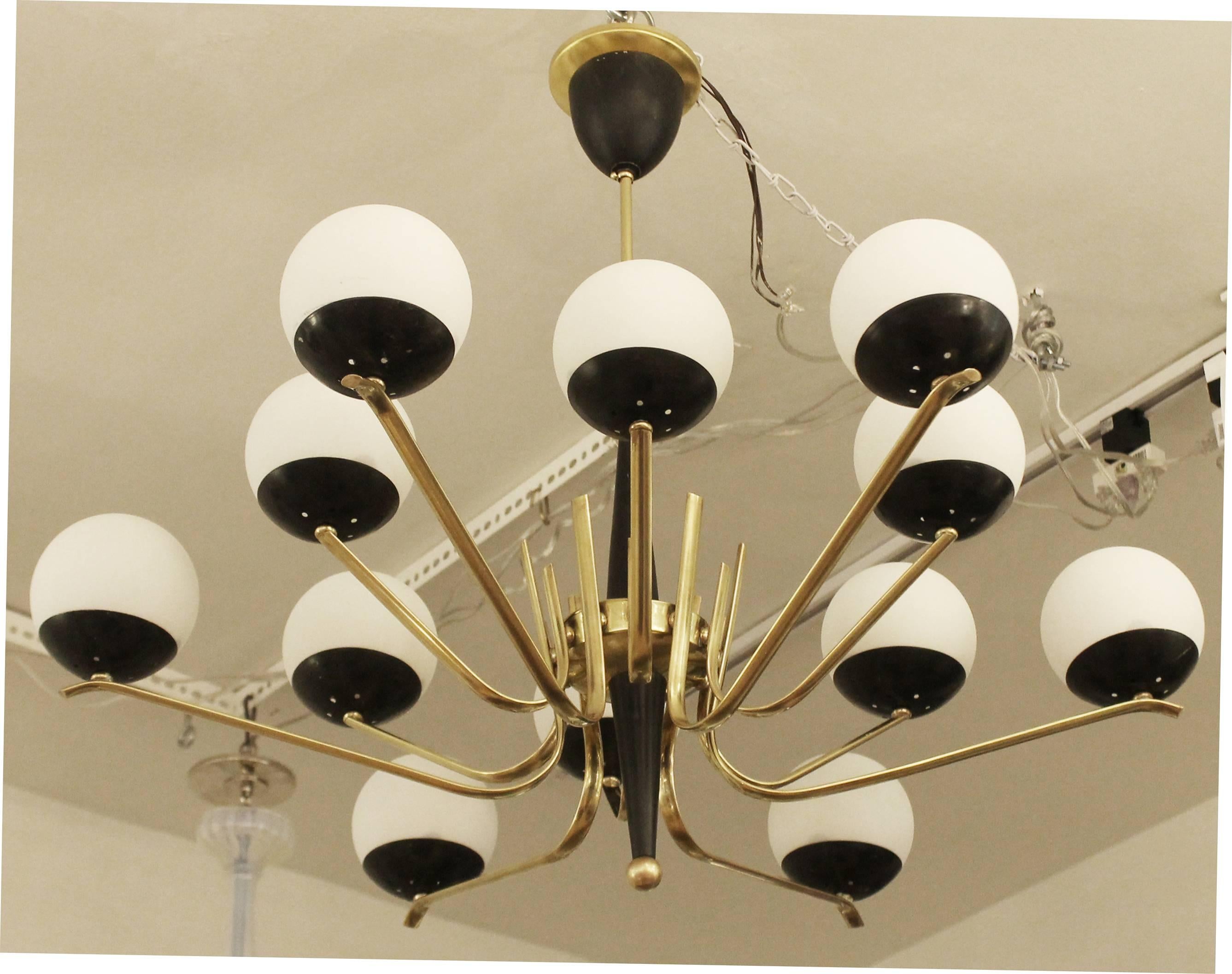 Impressive Stilnovo style chandelier featuring 12 alternating long and short brass arms. Each arm holds a black cup with a white frosted glass shade. Height of stem can be adjusted upon request. Holds 12 candelabra sockets.

For best pricing