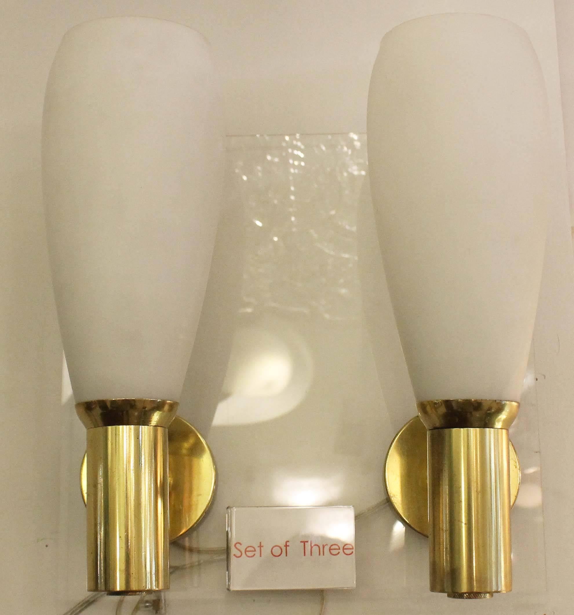 Set of three 1940s-early 1950s sconces featuring a brass wall mount sustaining a white sanded glass shade. The inclination of the front section can be adjusted. They can also be sold as a single or a pair.