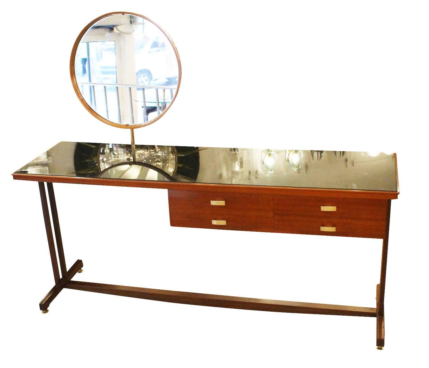 Beautiful Mid-Century wood vanity with a black glass top, round adjustable mirror and brass details. The mirror can be removed so that it can be used as a narrow desk. Color of finish can be changed at an additional cost.