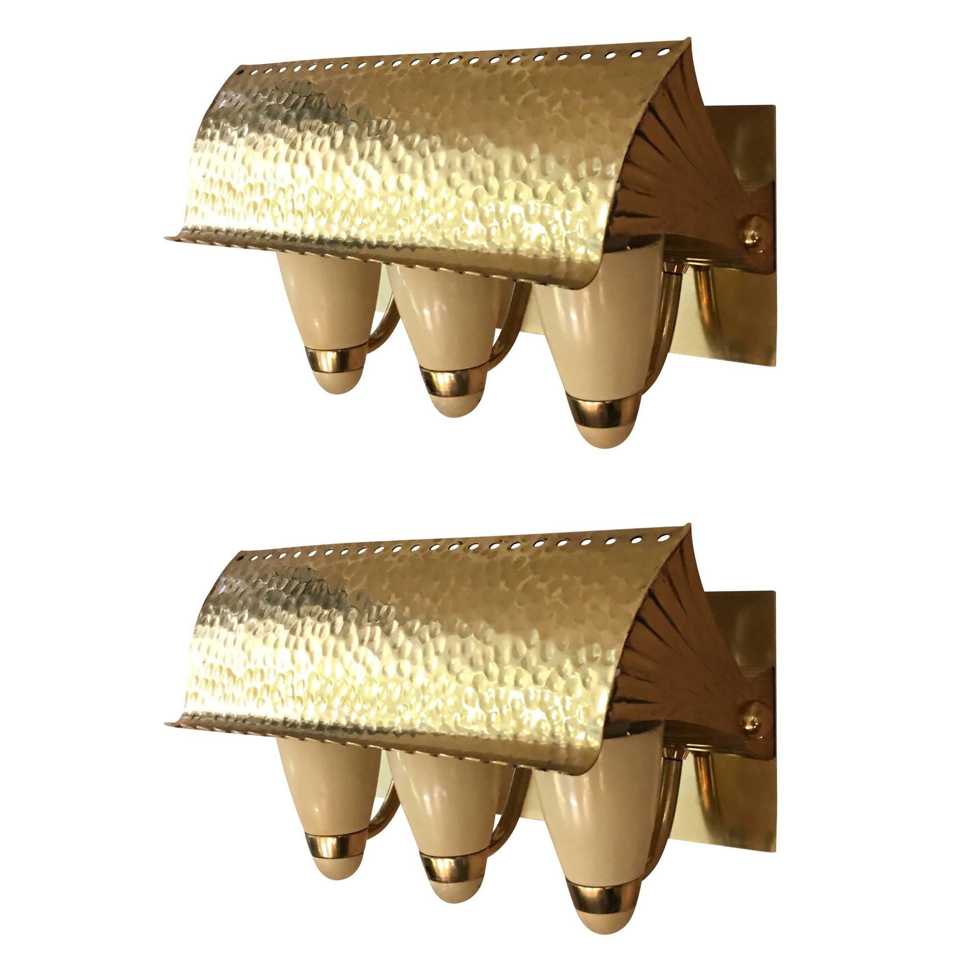 Elegant pair of Italian Mid-Century brass sconces featuring three off-white cones that hold the light bulbs and an adjustable hammered shade.
