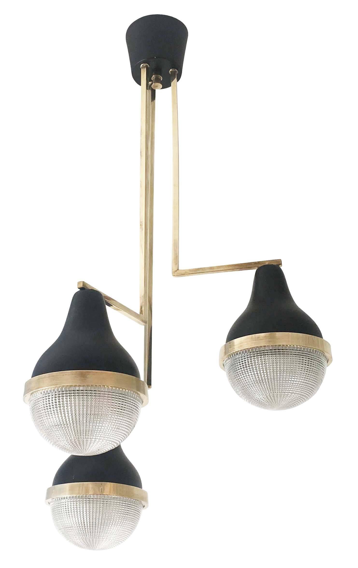 Diminutive Stilnovo chandelier featuring three glass shades at staggered heights. The glass is clear, pressed in a mold creating a texture that hides the light bulbs. The frame is brass a black lacquered aluminium. Ideal for a kitchen or entry.