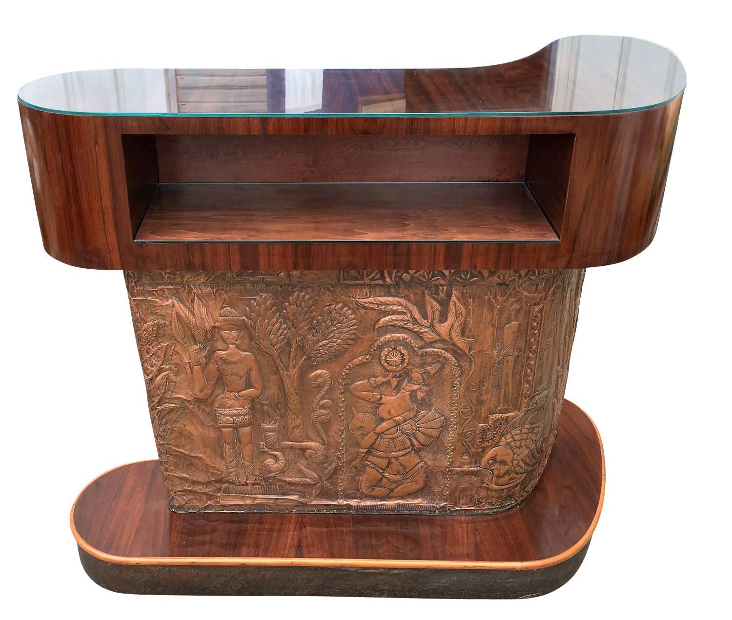 Extraordinary Mid Century dry bar counter which has a beautifully decorated embossed copper panel with a tribal motif that goes all the way around. The upper section is wood with an opening on one end and glass top. The base is also wood with a