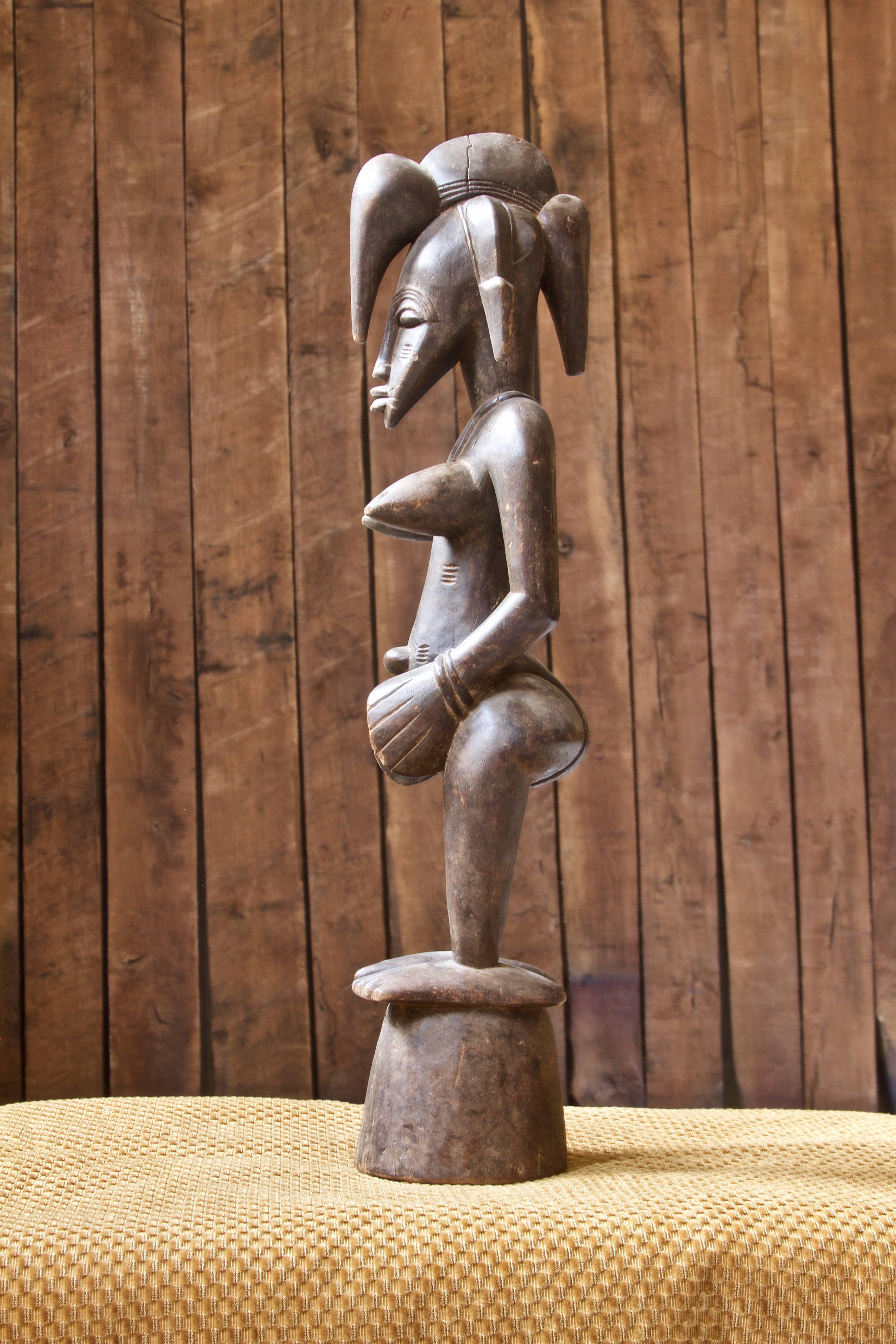 A female fertility statue of West African Senufo (Mali, or Ivory Coast) origin in solid wood. Hand-carved from a single piece of Mango wood, this expressive figurine features notch carving and a pedestal base typical of the sophisticated work of the