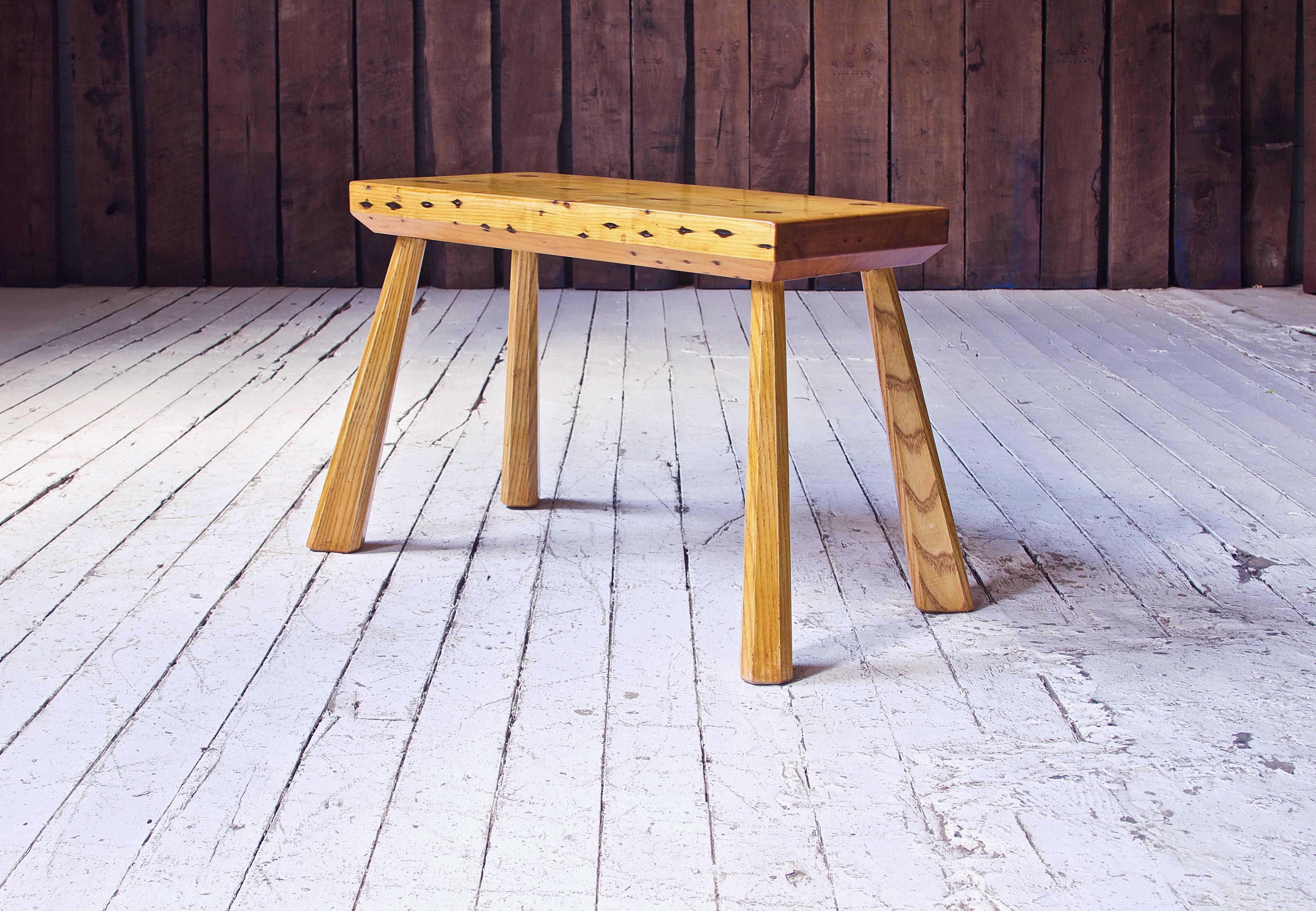 A rustic bench in Reclaimed White Pine and Ash inspired by the simple yet graceful furniture of the early American settlers. This type of archaic construction; tapering, chamfered splayed legs wedged through a slab top, was very common within