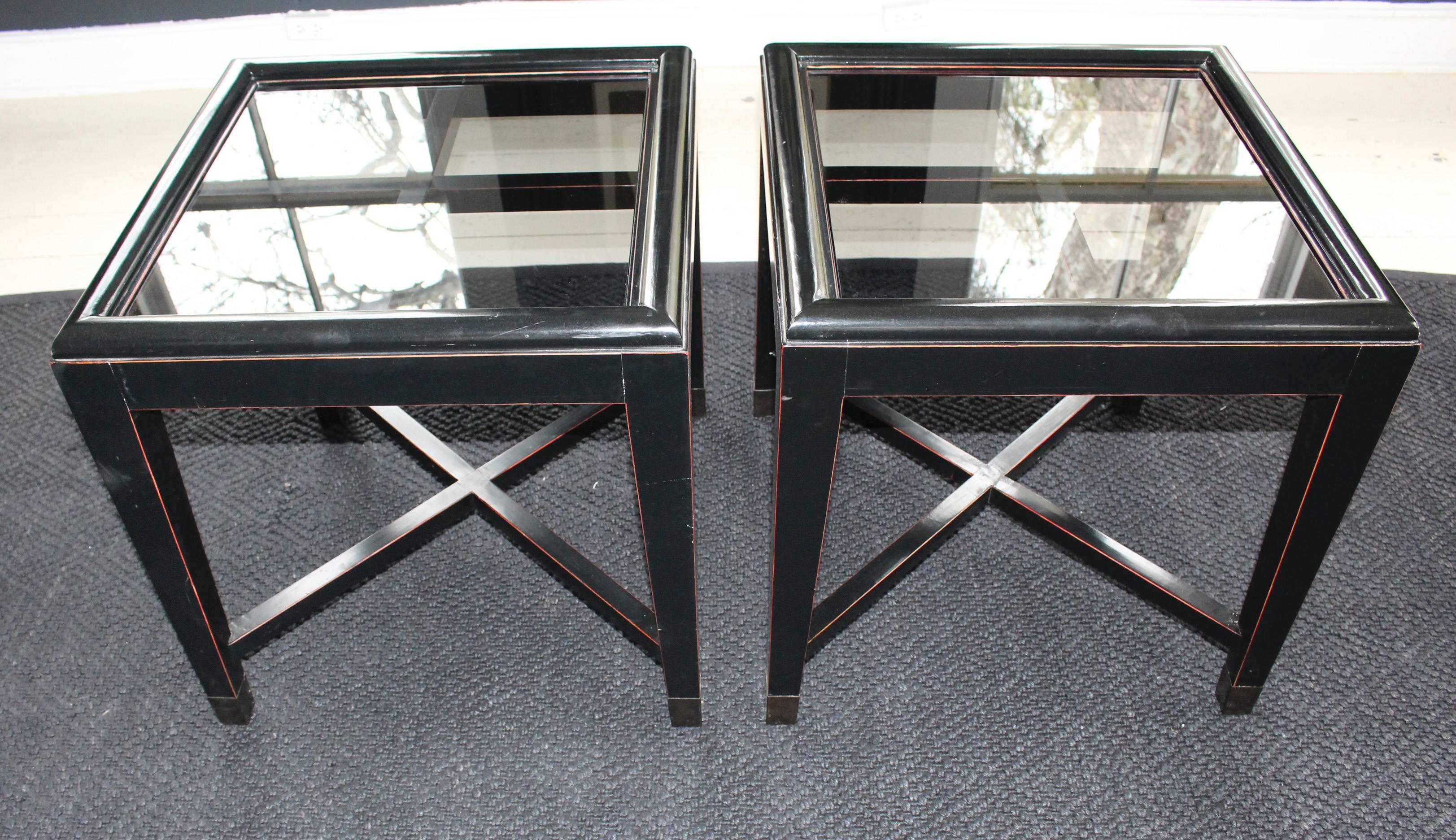 Pair of ebonized tables, late 20th century, with recessed glass tops are further distinguished with elegantly tapered legs wrapped with brass sabots and X-stretcher base. Tables are finished in a Classic asian two-tone technique with ebony over