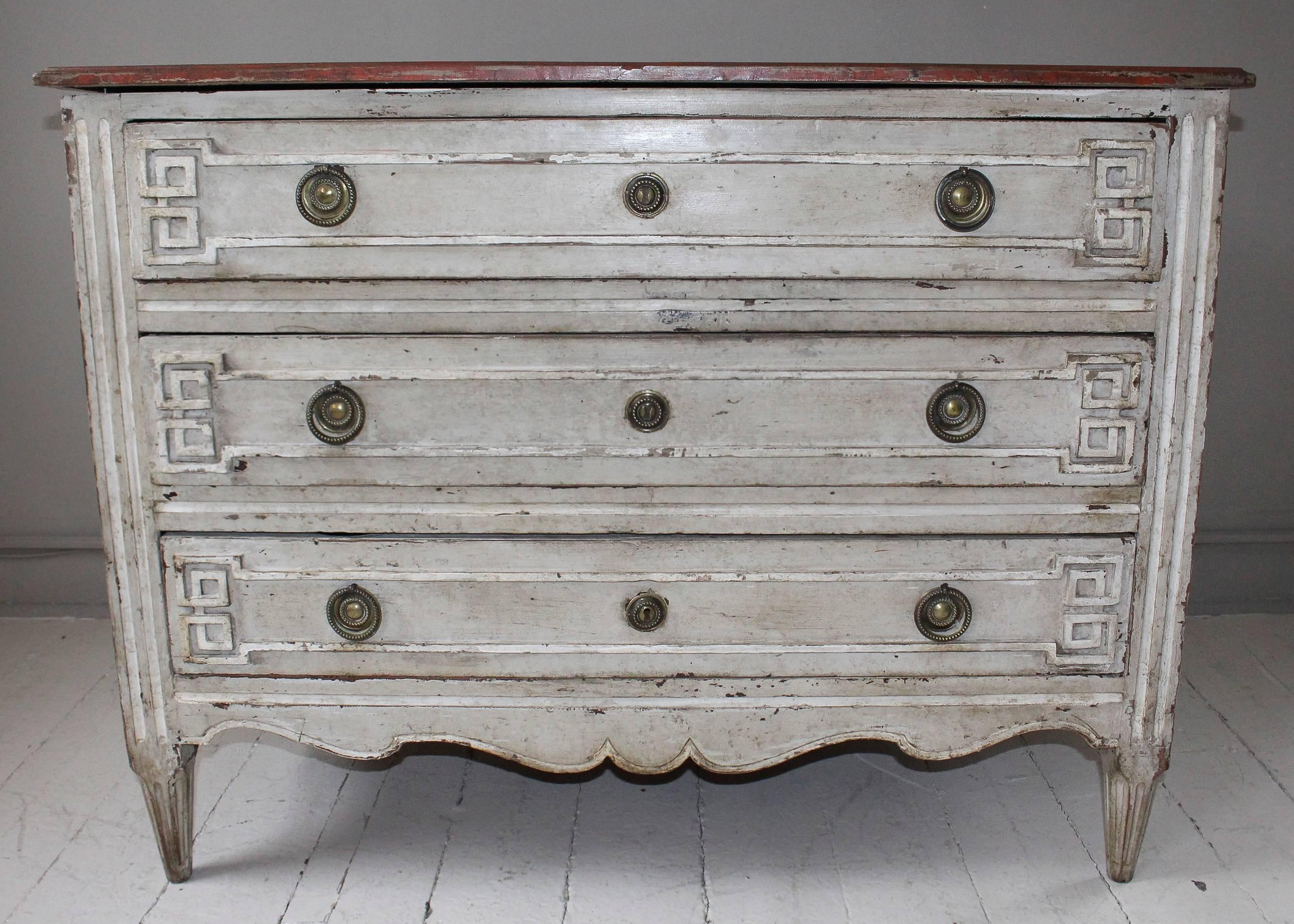 Painted commode, 19th century France, with three drawers having carved Greek key decoration. Commode is in distressed oyster paint with red mottled painted top. Brass fittings and carved scallop apron lends further charm.