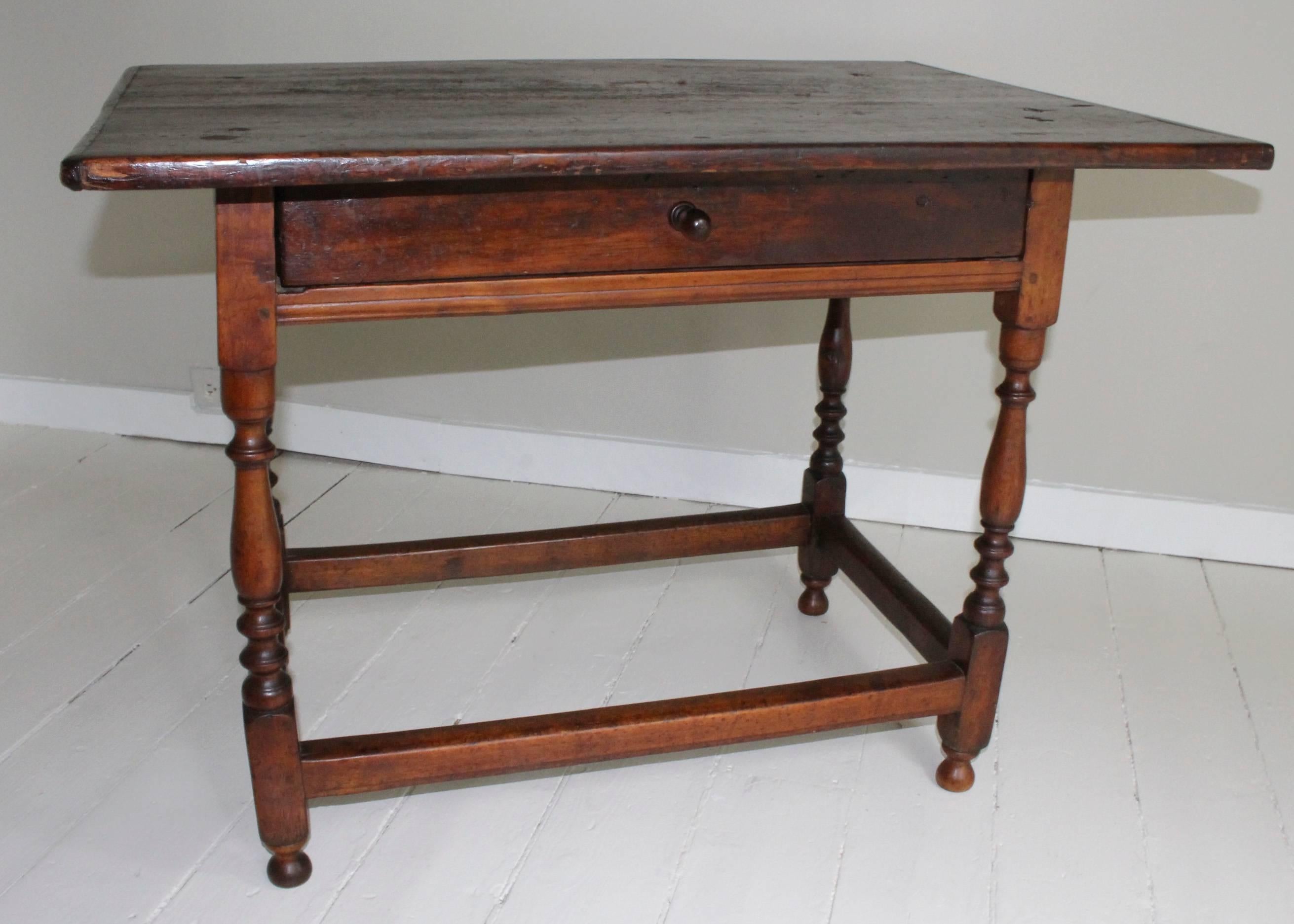 Refined 18th century American oak tavern table on turned wood legs joined by stretcher supporting a broad plank top with wonderful time-worn patina. Single drawer distinguished by Novel Elongated Pull.