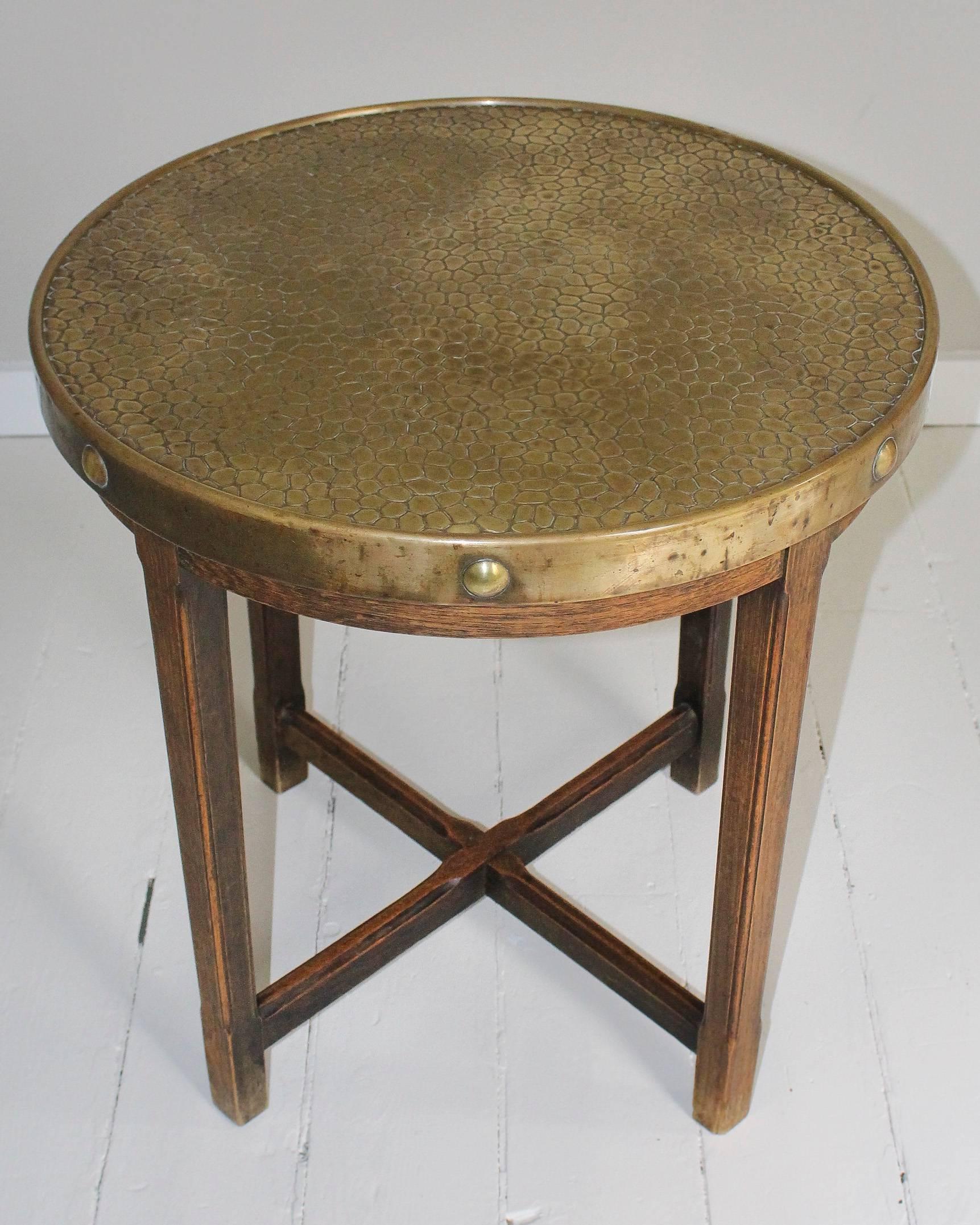 Circular table, 1920s, France, with pressed brass top in a crocodile pattern secured with giant rivets atop an oak cross-stretcher base.