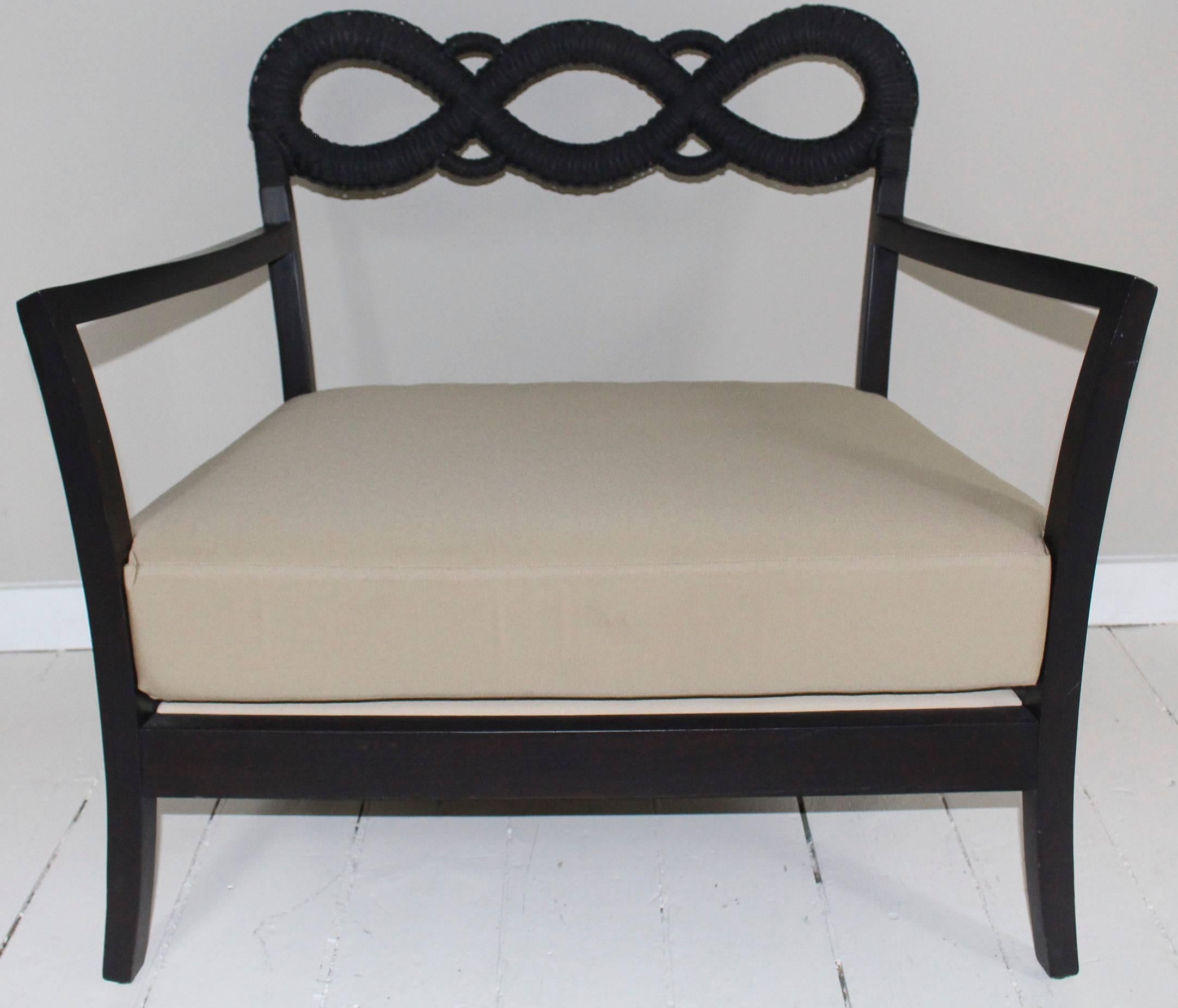 Ebonized oversized side chair with decorative rope backrest and outward slanted armrests. Chair is wider, deeper and lower than the usual seat. Neutral seat cushion with similar flange-edged lumbar back pillow.