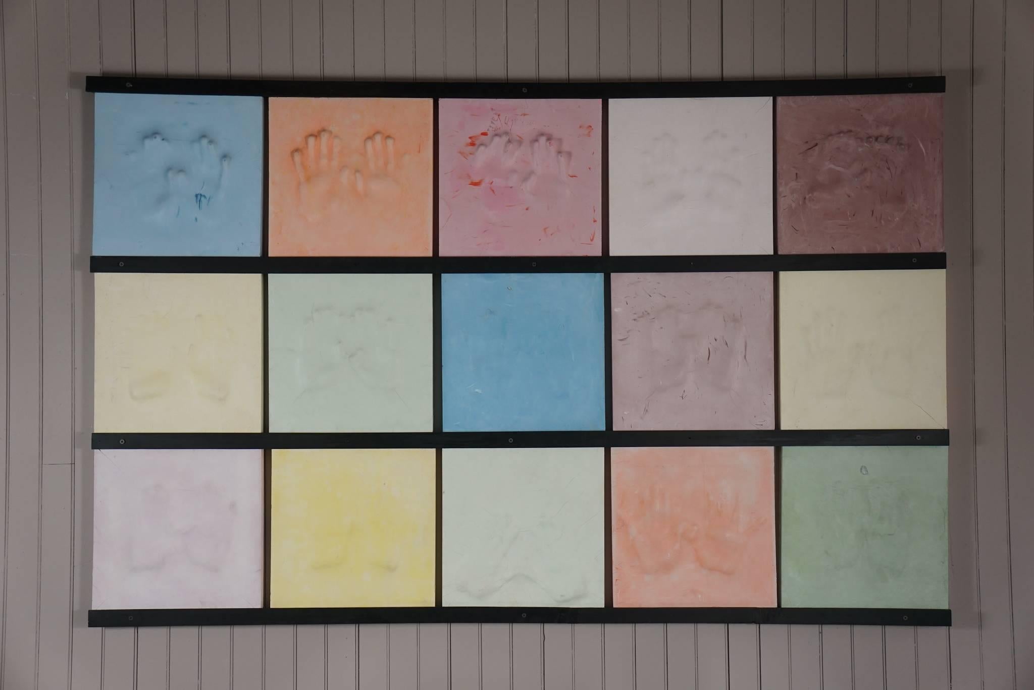 15 hollow plaster blocks of hands, in various pastel colors. Set on wooden strips attached to the wall.