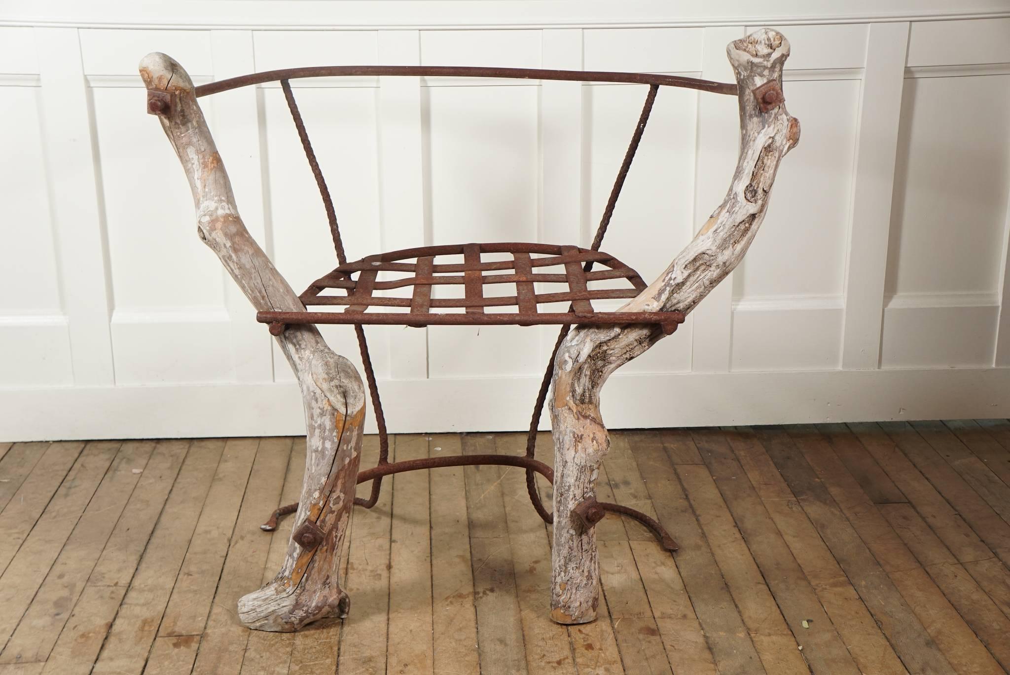 Organic chair designed with gnarled wood branches woven-wrought metal seat, metal rod back and legs ending in a flourish all attached with large square nuts.