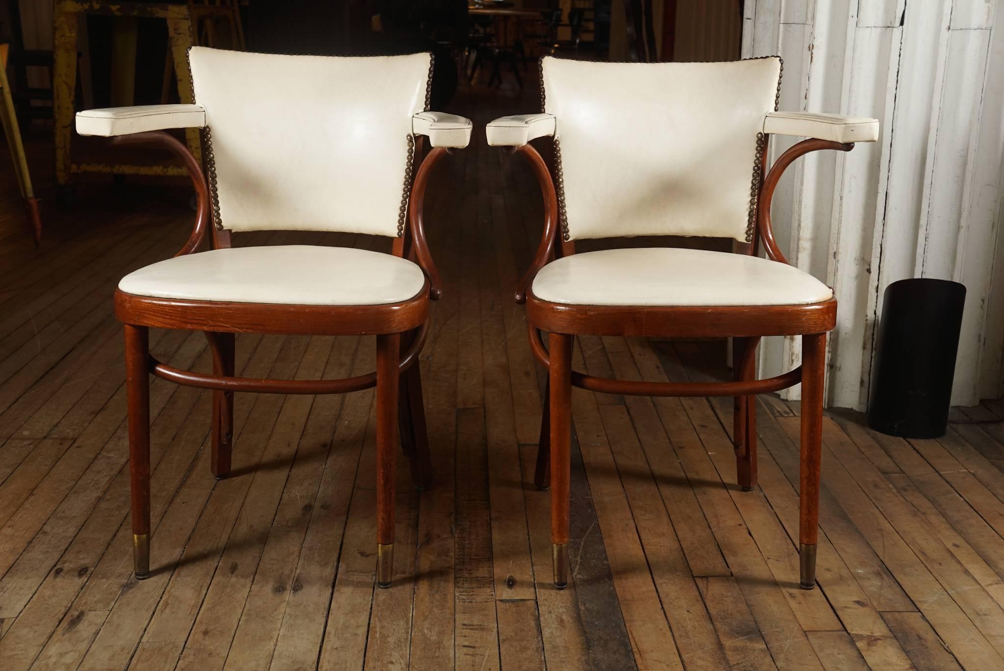 Pair of bentwood Thonet armchairs upholstered in an off white leather, brass tack trim, brass sleeves on front feet.