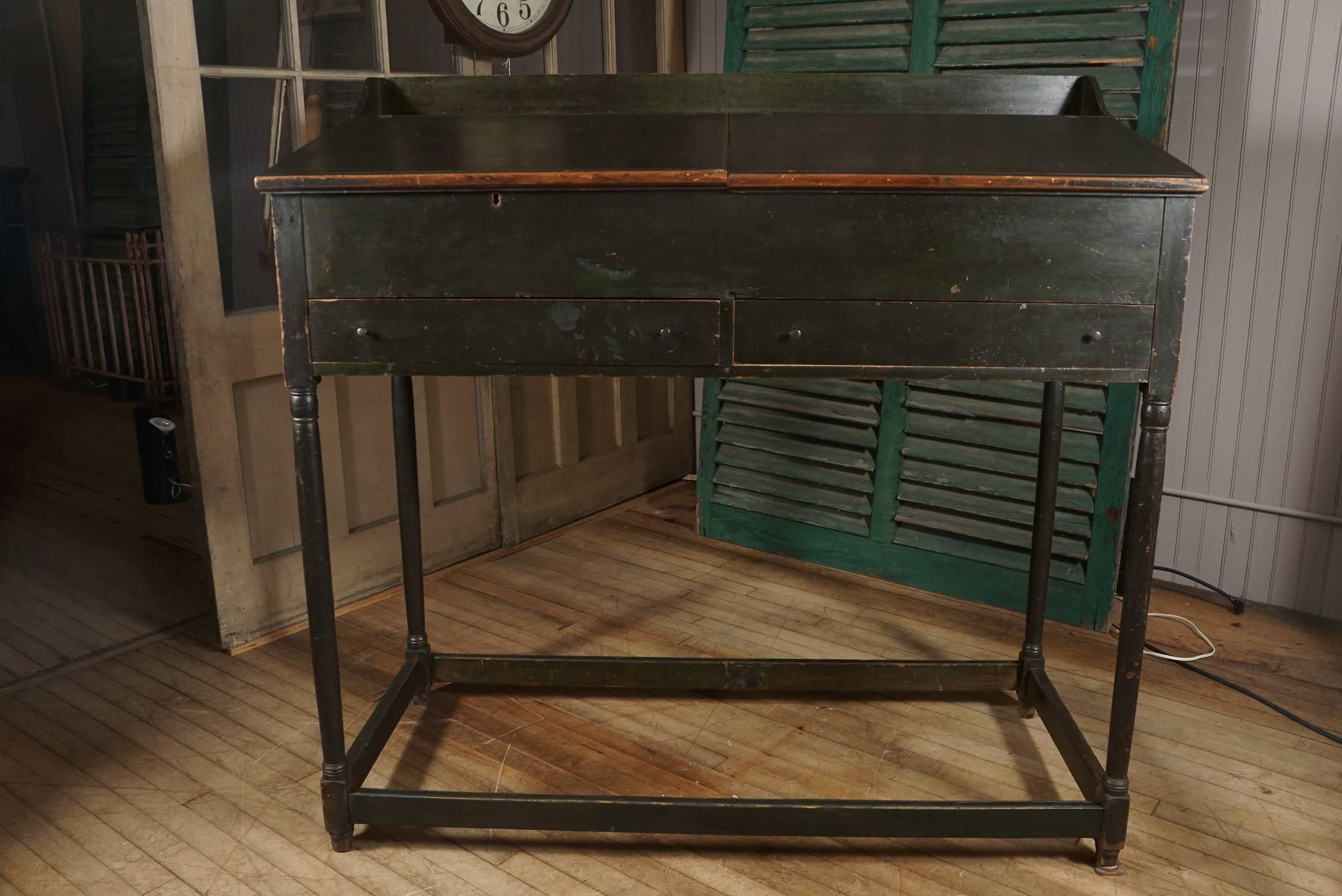 early 19th c New Hampshire partners desk - two breadboard end angled lift lids - one with lock - reveal storage area with cubbies - surmount two drawers - dovetailed gallery - delicately turned stretcher base - in original bottle green paint with a