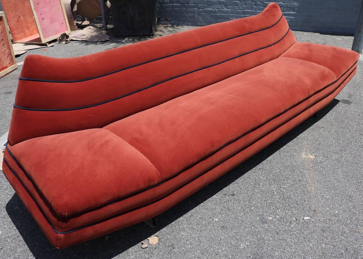 Long orange velvet sofa with navy piping from the 1970s with wooden legs.