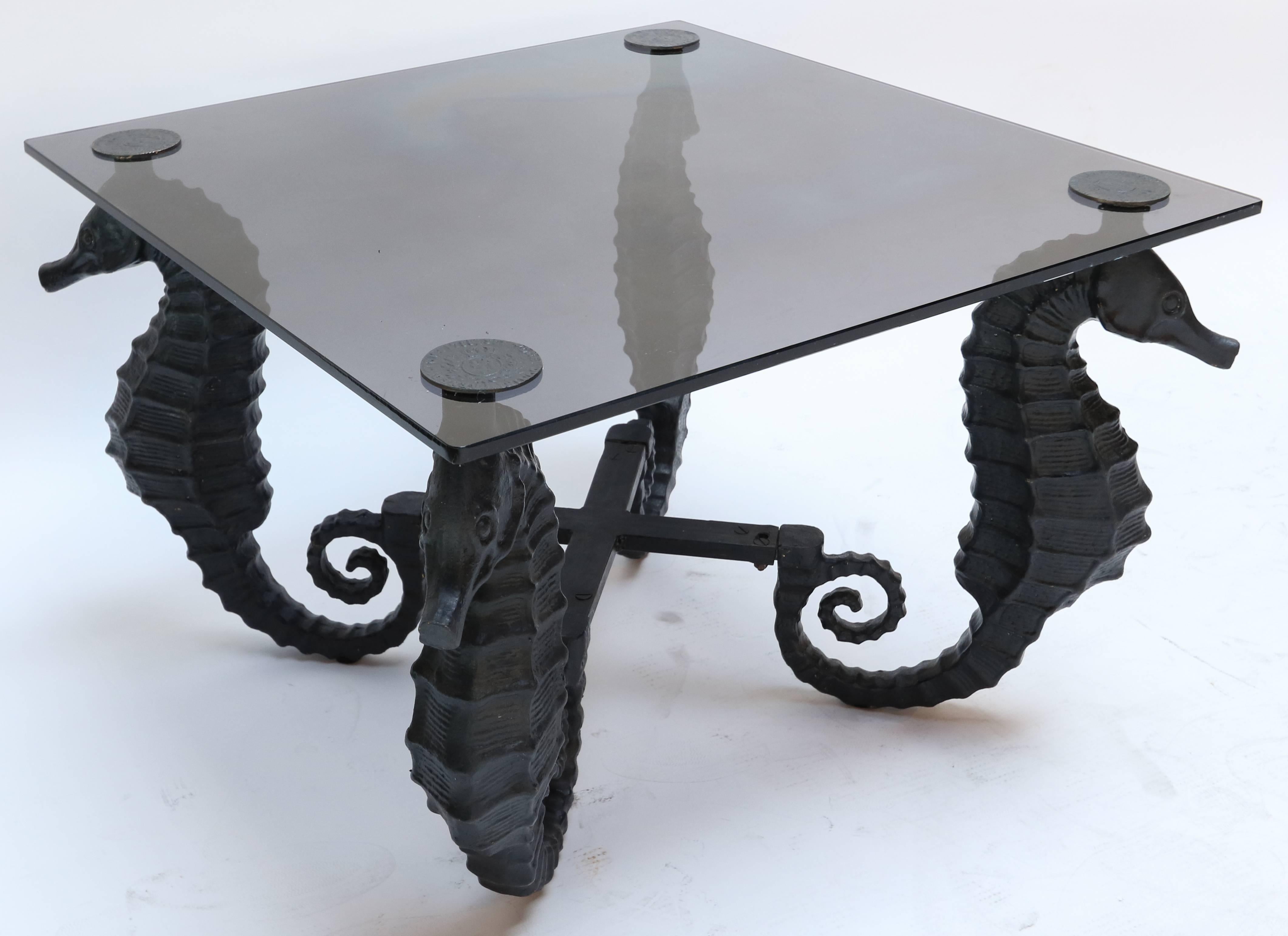 Pair of black iron seahorse side tables with smoked glass tops with brass medallions.