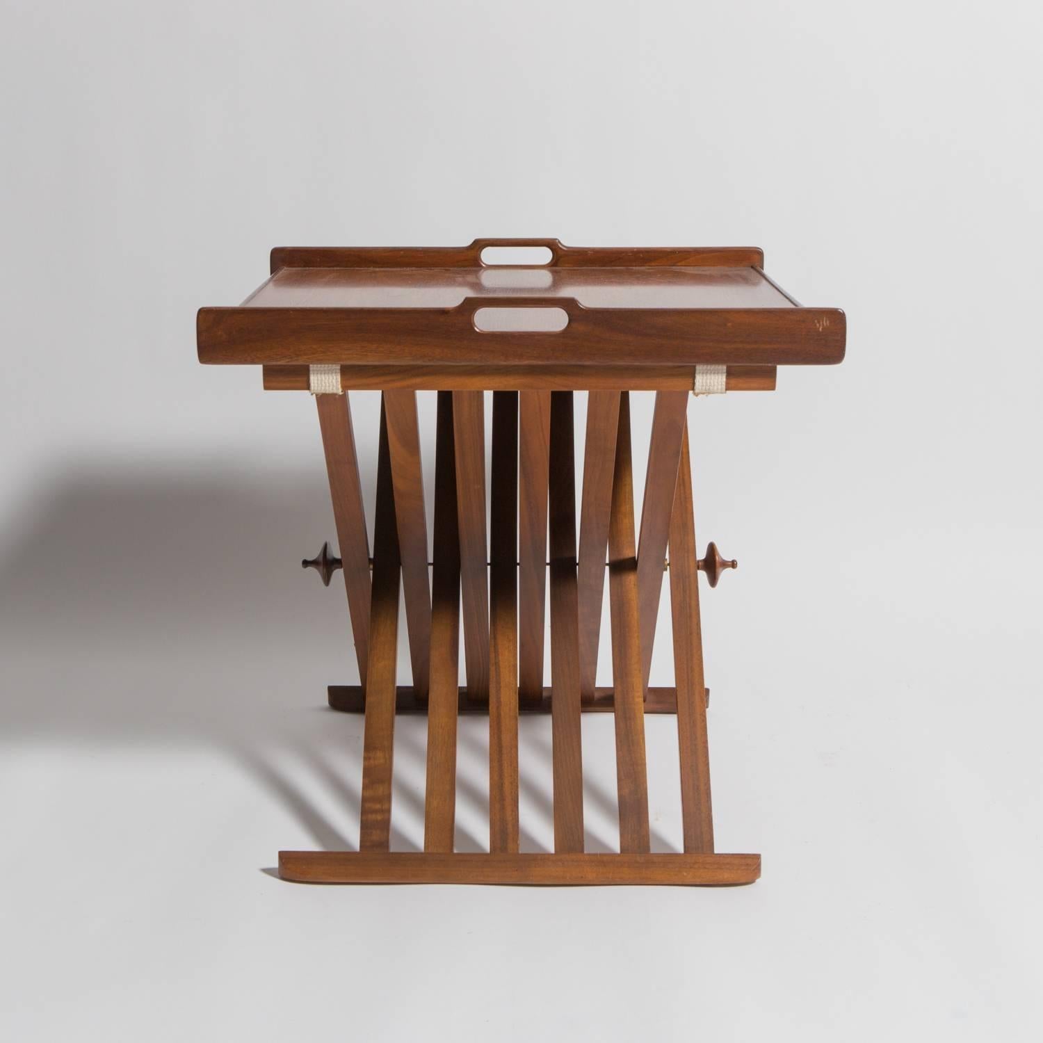 Pair of walnut folding Campaign tray tables by Stewart MacDougall for Drexel. Removable tray top with carved handles and elegant touch finials at the leg axis.