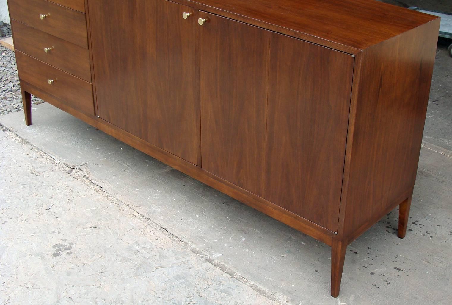Gorgeous 12-Drawer designed by Paul McCobb for Calvin. Walnut cabinet with original brass pulls.  Restored finish.  The bank of drawers on left side features pop-up vanity mirror. To right are double bi-fold doors with 8 pull-out drawers behind.