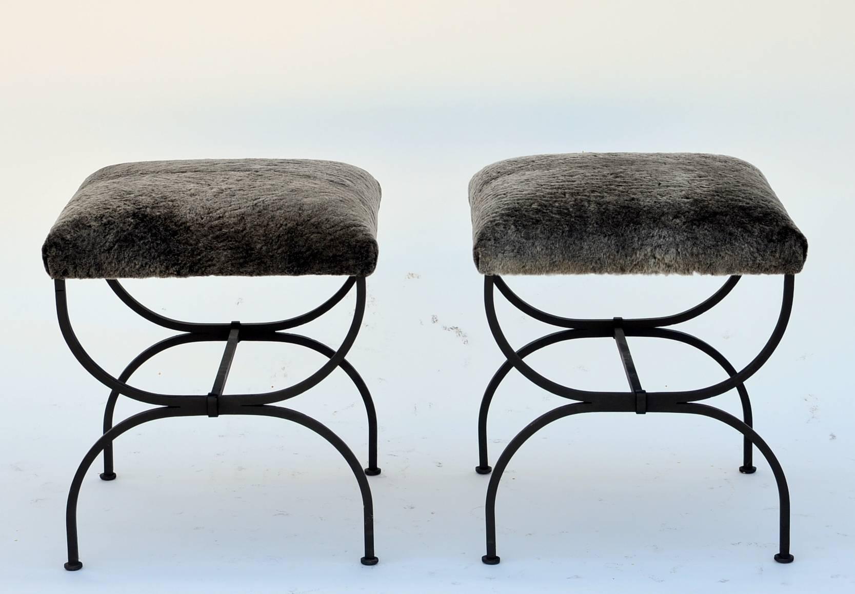 Pair of chic fur-covered wrought iron stools in the style of Gilbert Poillerat. Upholstered firm. Great in front of a coffee table or a fireplace in the living room or at the foot of a bed instead of a bench.