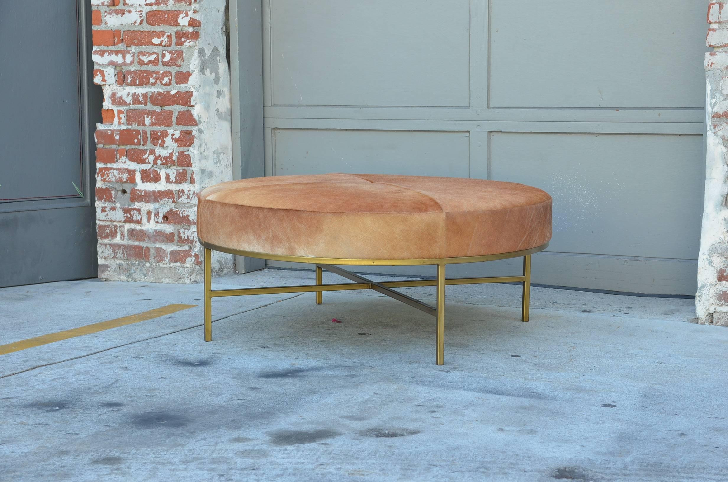 Our chic 'Tambour' natural hide and brass round ottoman is perfect to use in place of a coffee table. Natural cowhide upholstery over antiqued brass base. Upholstered firm so it can be used to sit, relax the feet, and as a coffee table for books,