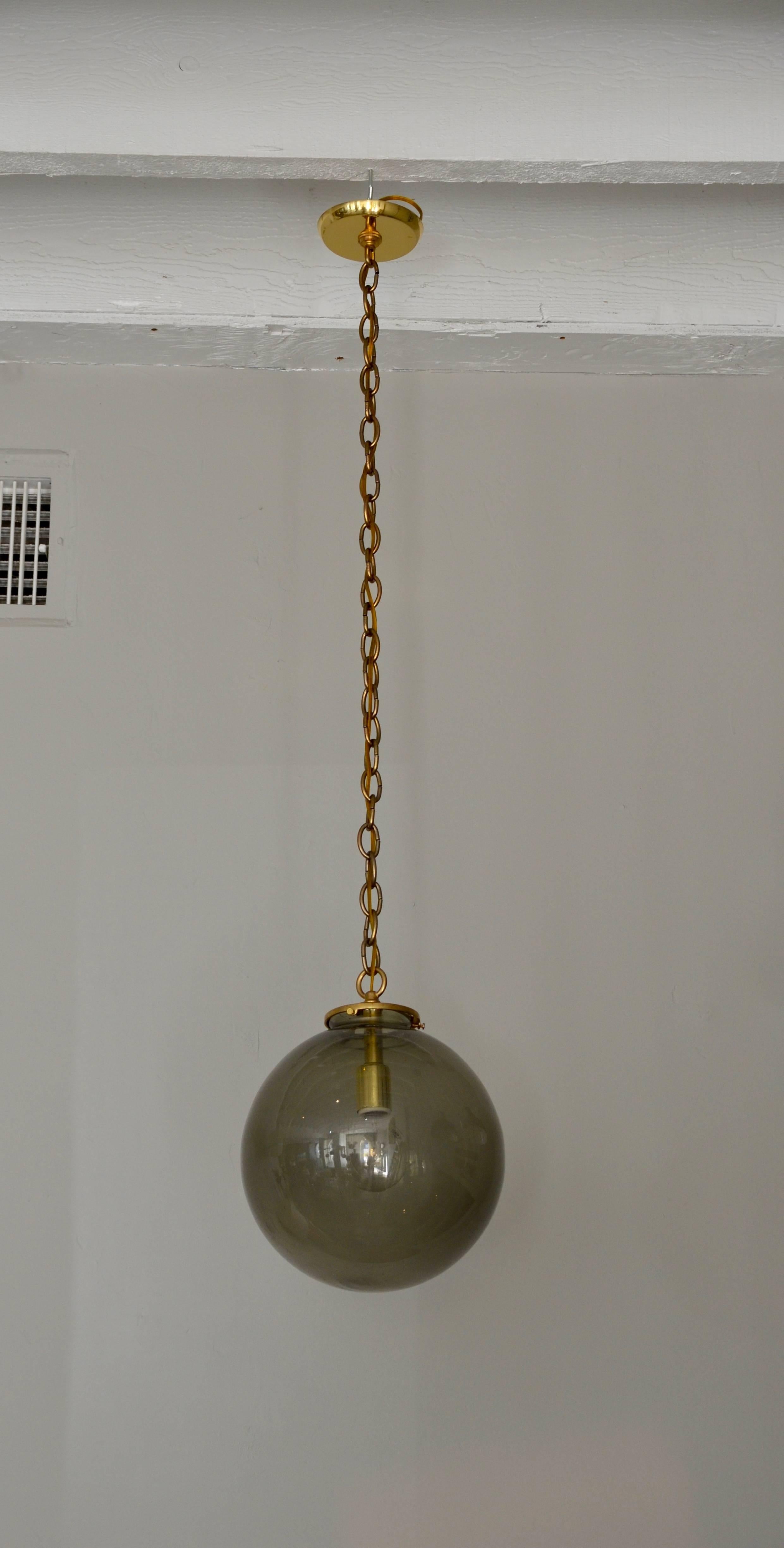 Pair of smoked glass midcentury globe lights. Brass fittings. Matching chain and canopy included. Chain length can be adjusted.

The last picture is to give an idea in setting. But they are not the exactly the same lights.