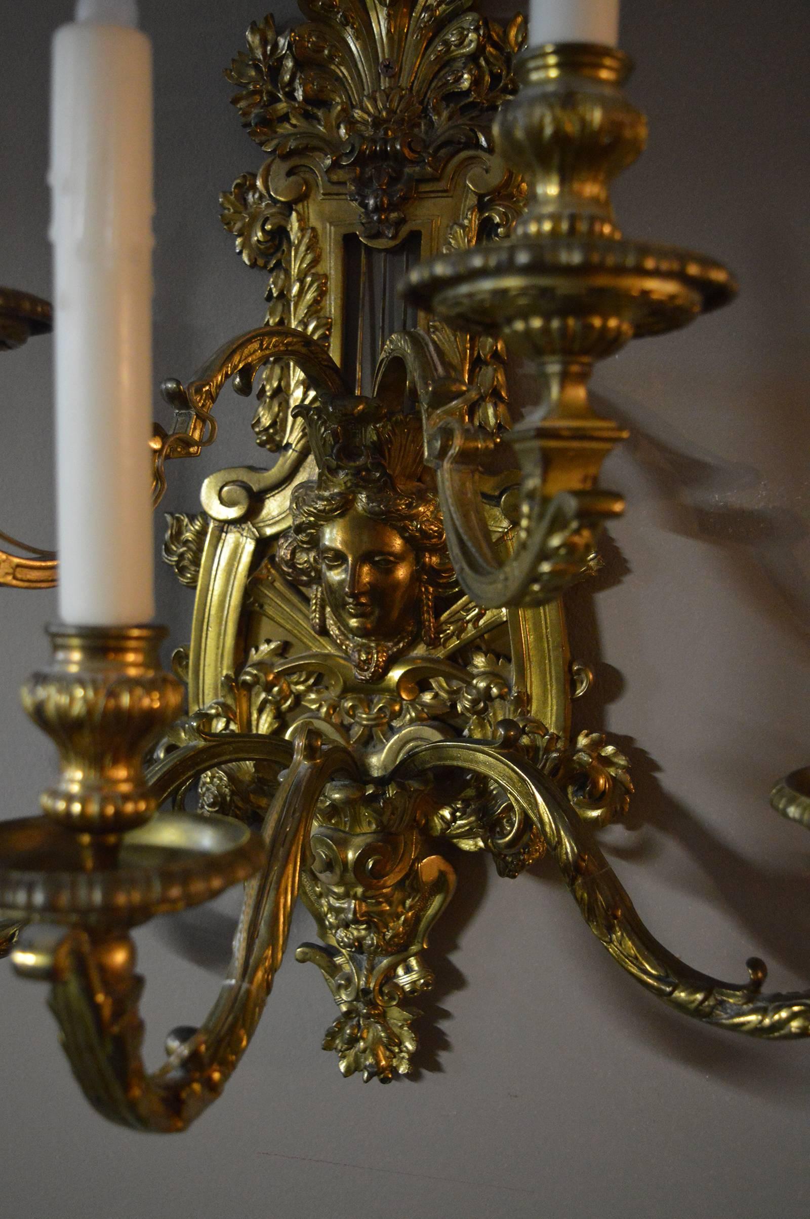 Pair of detailed brass sconces. There is a female face at the centre of the sconce and a male face at the bottom.