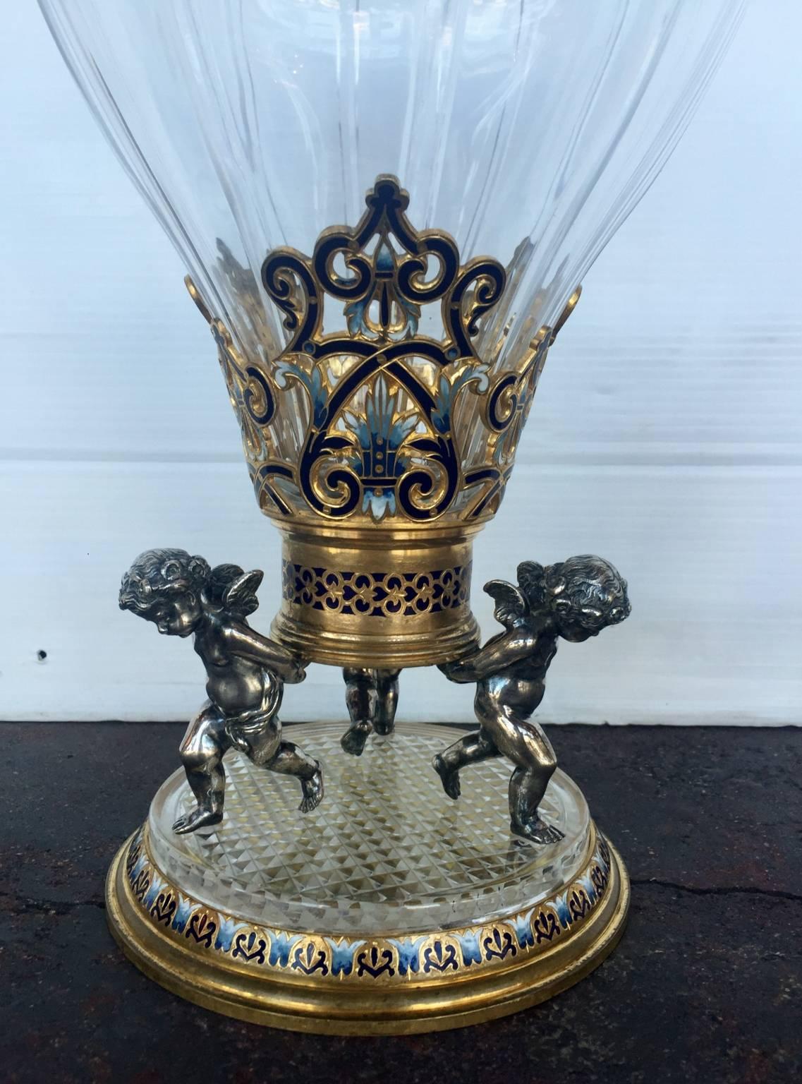 19th century French 19th century French Champlevé enamel and Baccarat glass vase. The base of the vase has three cherubs supporting the structure of the glass vase with champlevé enamel. Enamel and Baccarat glass vase.