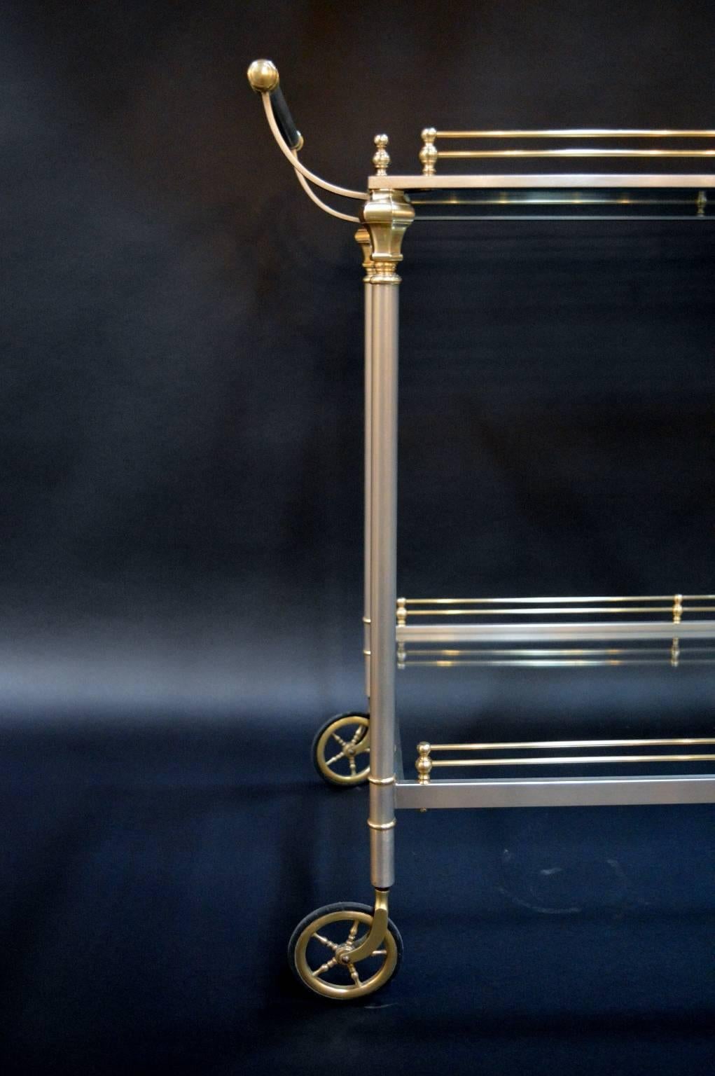 Gold and silver metal bar cart with two glass shelves in the style of Maison Jenson.