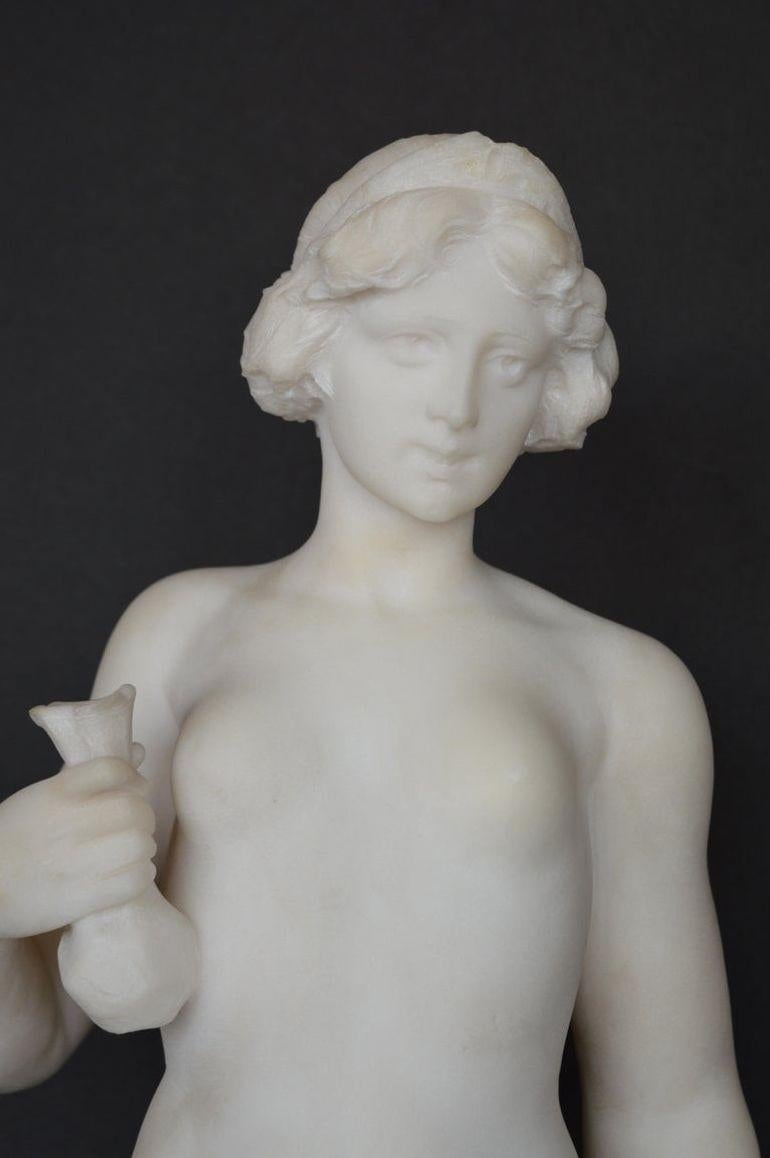 Una statua in marmo di Carrara, delicata e splendidamente scolpita, che raffigura una giovane ragazza seminuda che tiene un bouquet di rose in una mano e un vaso nell'altra. Questa scultura italiana della fine del XIX secolo cattura l'eleganza