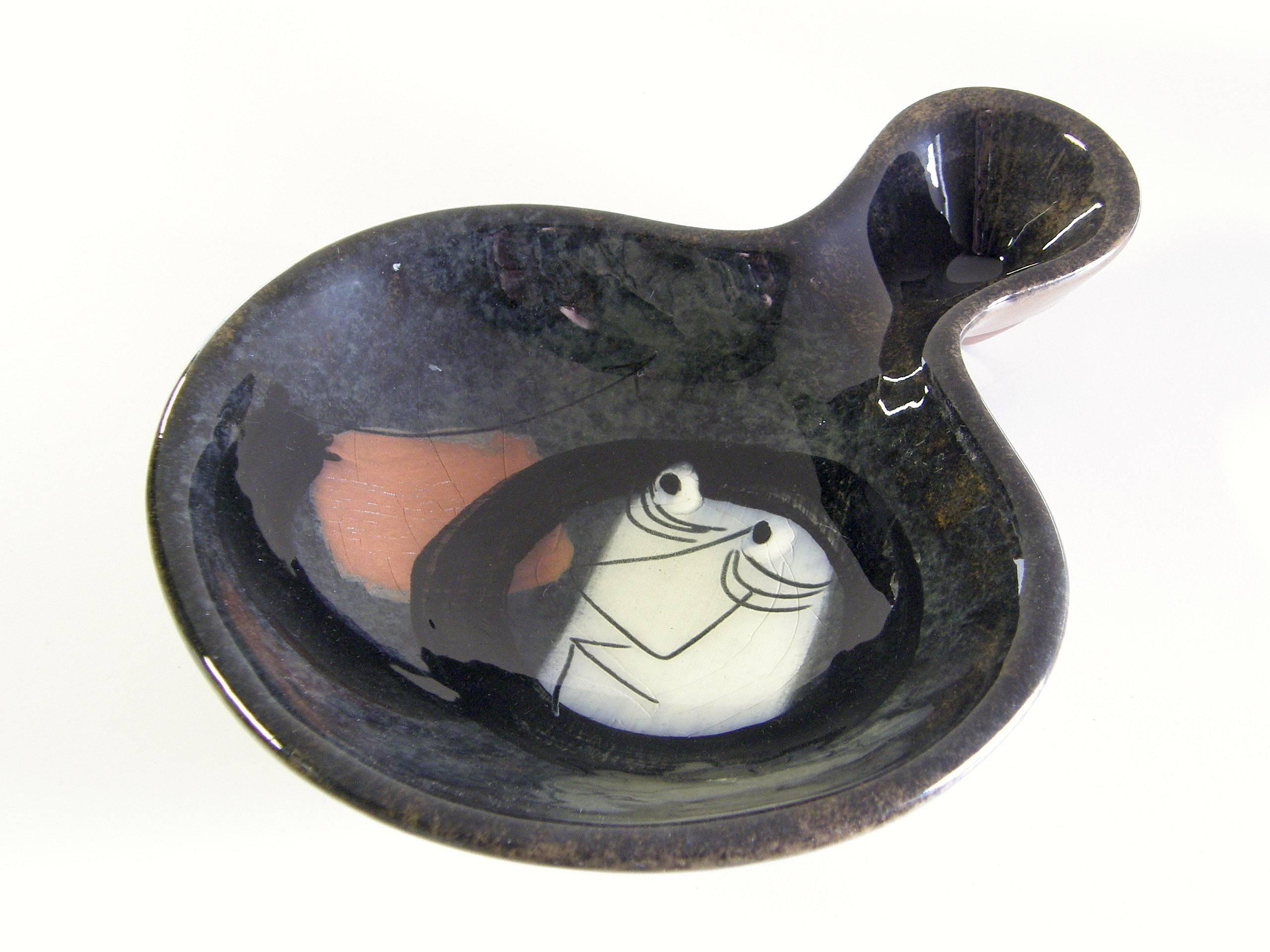 Cet amusant plat en céramique du potier californien Edmund Ronaky a une forme libre et une forme en deux parties. Il est recouvert d'une glaçure brillante sur un motif représentant un homme à l'air inquiet qui semble être un Esquimau avec une