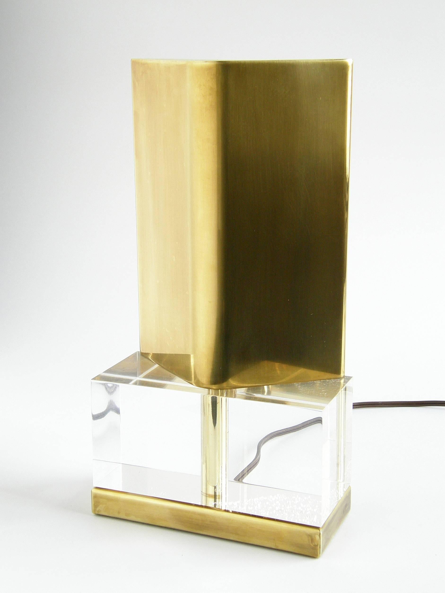 This simple reflector lamp has a rectangular Lucite cube base with a brass foot and a tent-shaped brass shade. It gives a subtle, indirect light and would make an excellent accent lamp within a shelf unit or on a table or cabinet top. It could also
