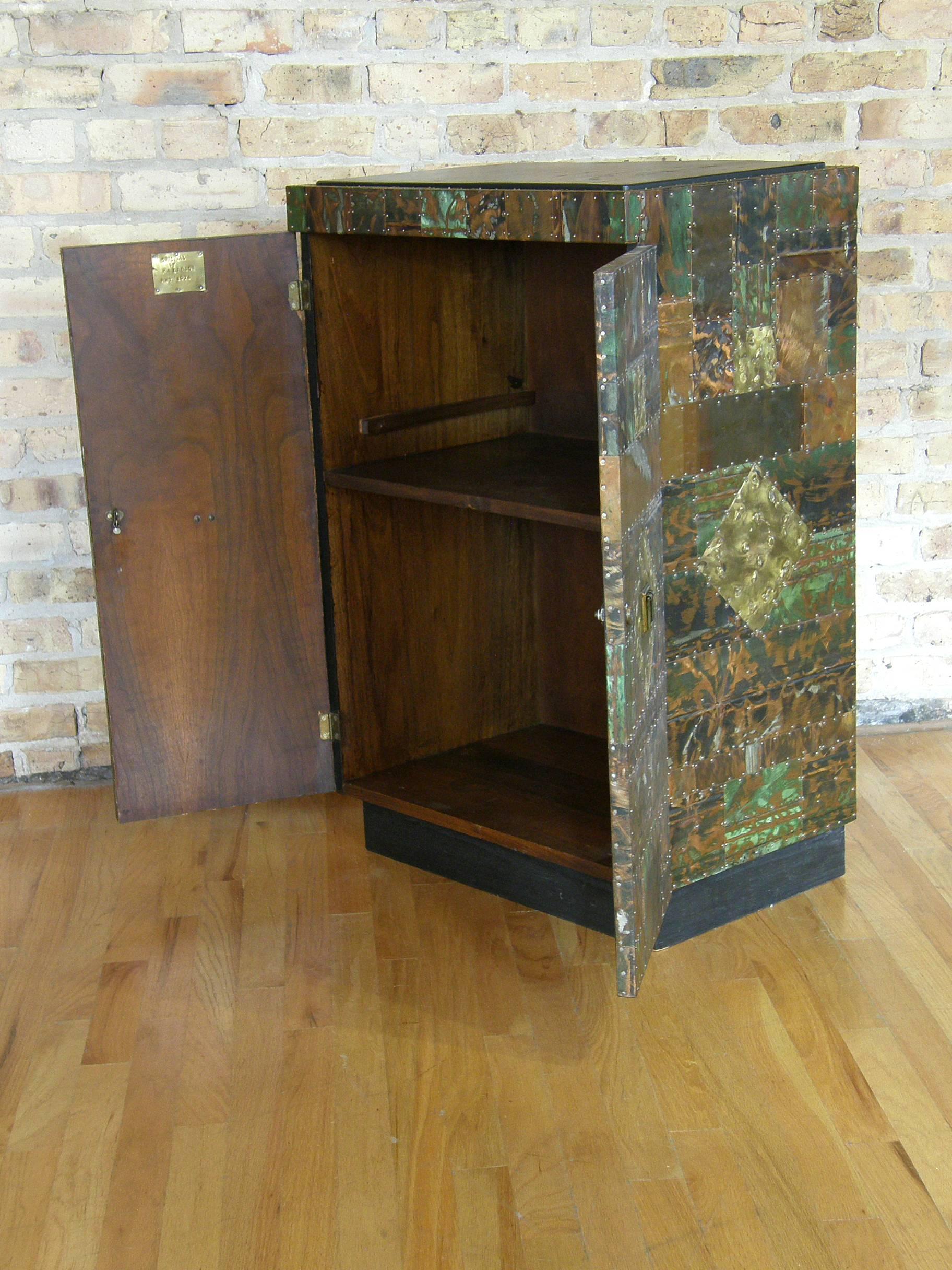 Studio made cabinet with patchwork copper and brass clad surface. The metal pieces are patinated and enameled with applied, torch cut, and ground down textures in the finish. The nailheads that attach the various pieces add a tactile and visually