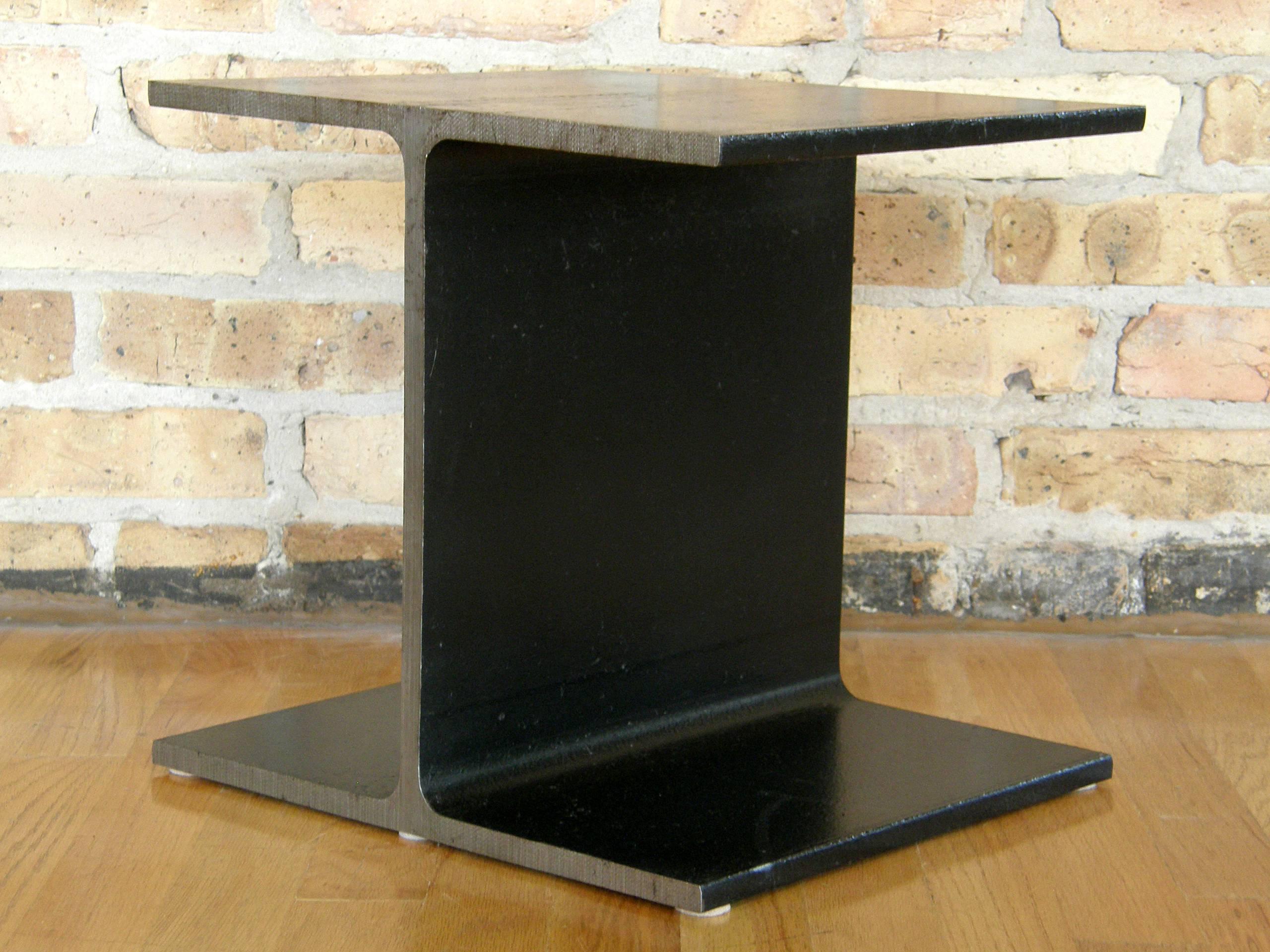 Minimalist side table in the form of a slice of an I-beam. The Classic Industrial form of the I-beam has been domesticated by removing it from it's context and bringing it to an intimate scale. The flat surfaces have a black enameled finish, and the