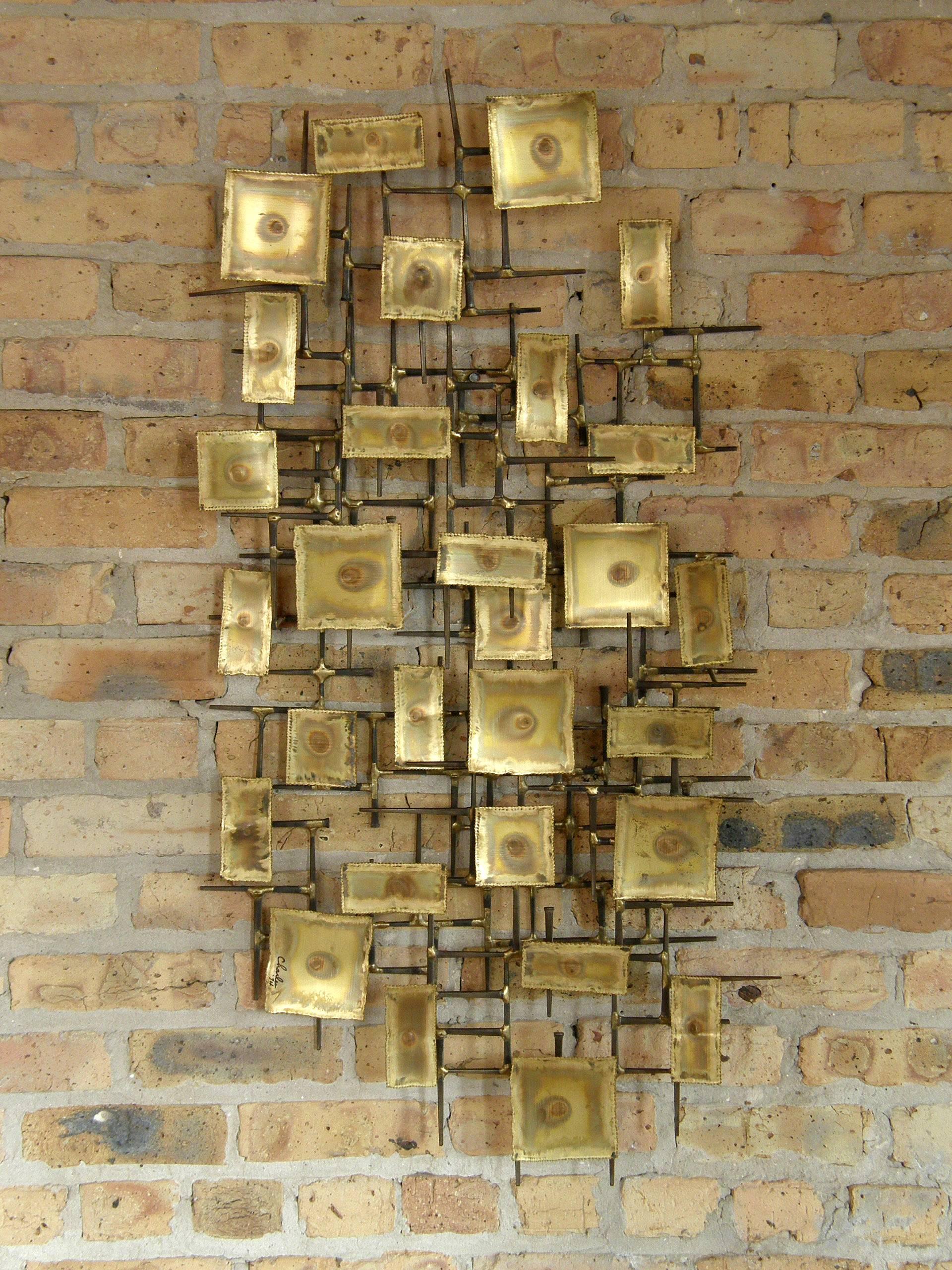 Three dimensional, brutalist wall sculpture with a frame of square nails set with torch cut and patinated brass rectangles. Signed 