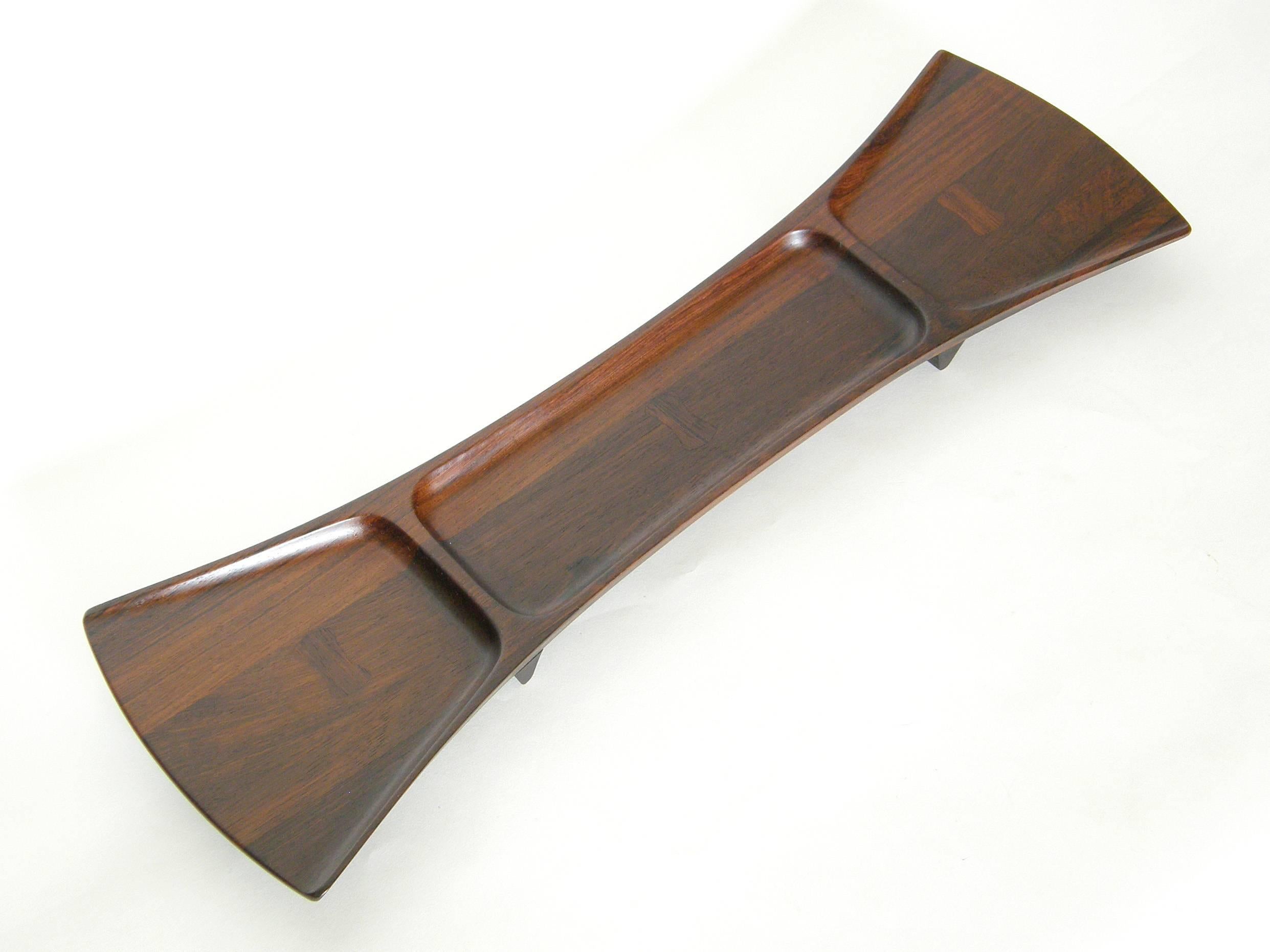 Tripart rosewood tray in the form of an elongated bow tie, designed by Jens Quistgaard for Dansk. The bow tie shape is repeated on the tray as little inlaid pieces running perpendicular to the grain. 

This tray, marked palisander (a type of