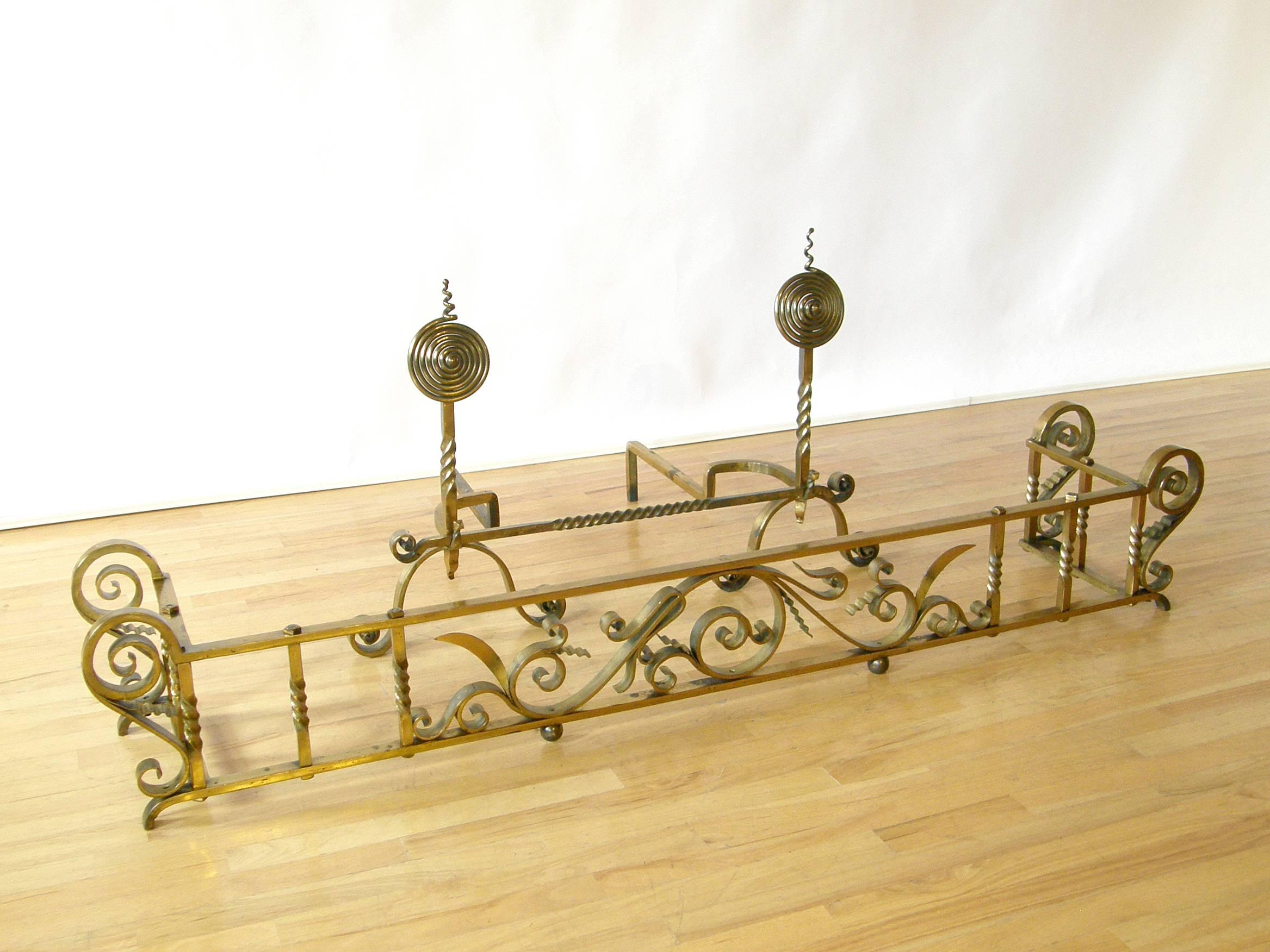 Brass-plated wrought iron fireplace set consisting of andirons with removable cross bar and fire fender. The set features twisted and coiled forms, elaborate scrolls and floral motifs. It has a nice scale and impressive presence.

Approximate