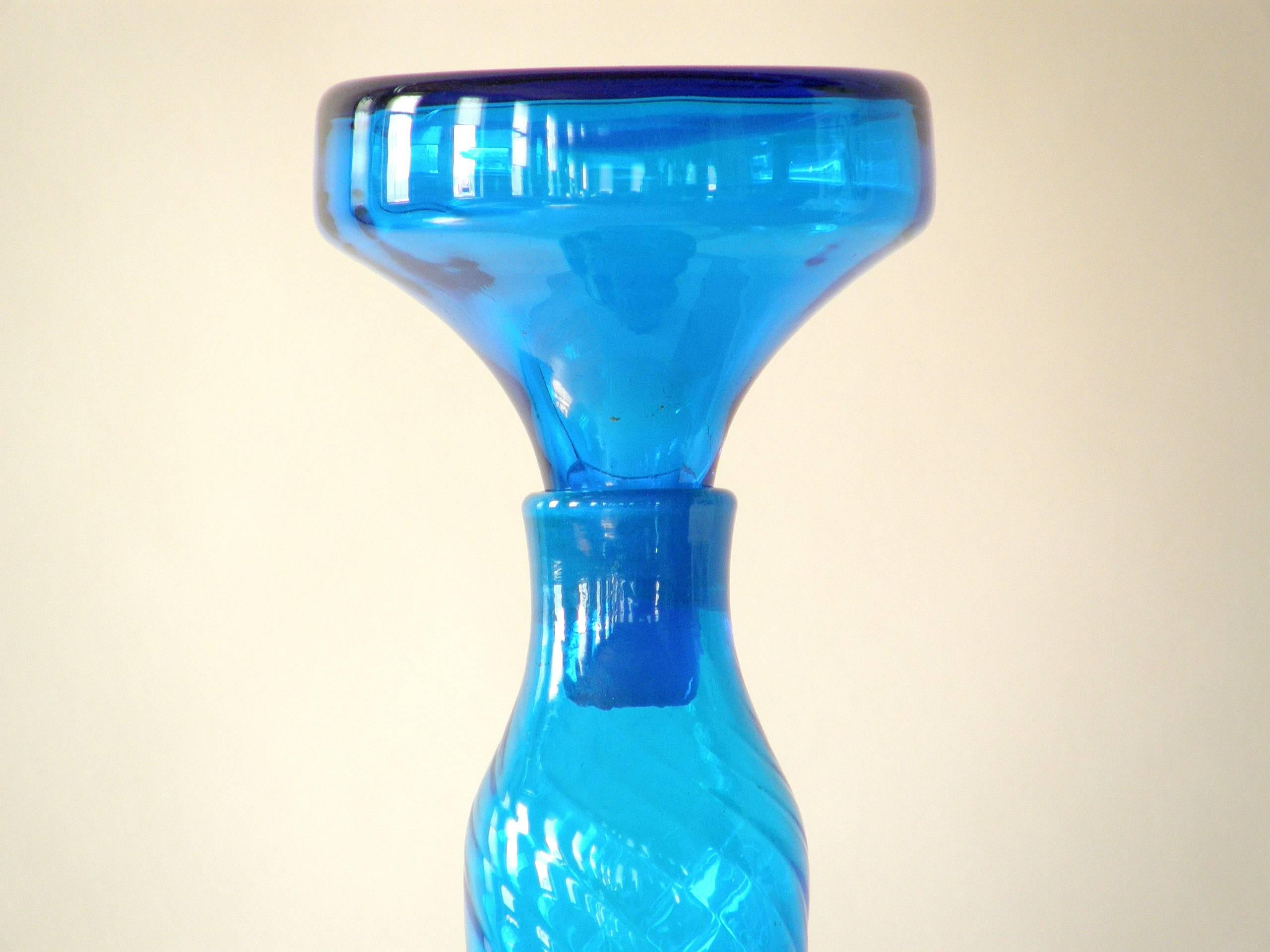 Tall, slender glass bottle in bright blue by Blenko. The bottle has a subtle effect of spiraling lines, and the stopper shape mirrors the shape of the base.

Please contact us if you have any questions.