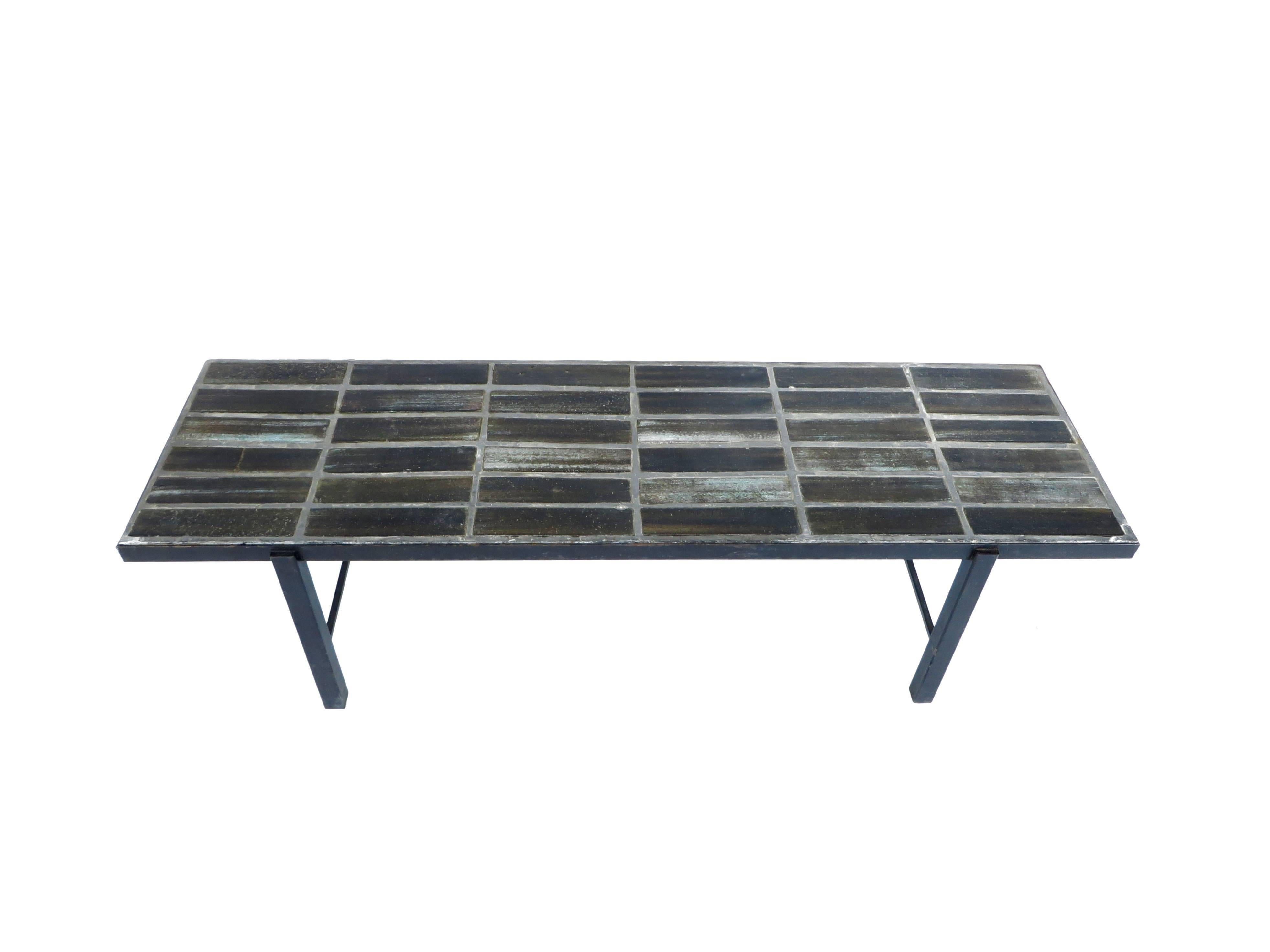 An impressive French, circa 1960s ceramic tile top coffee table on black lacquered iron base. 
The plateau is made of varying shades of blue, varying grays and black and touches of brown artistically glazed elongated tiles set in a dark cement.