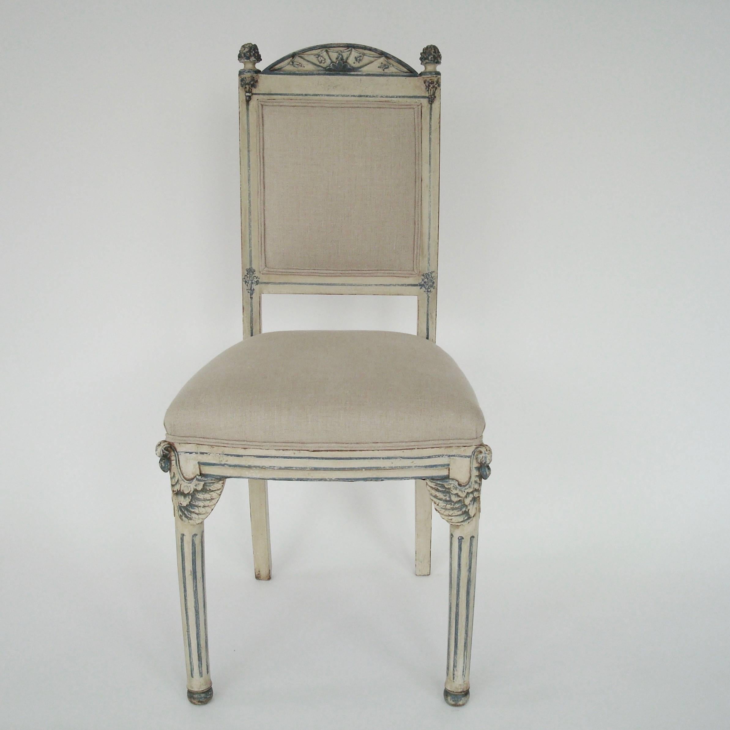A pair of Italian Venetian side or dining chairs in white grayish paint with blue details. Stylized swans in blue at the tops of the legs, sunburst pattern at the top of the chair with finials. 
Upholstered in natural linen, 
circa 19th century.