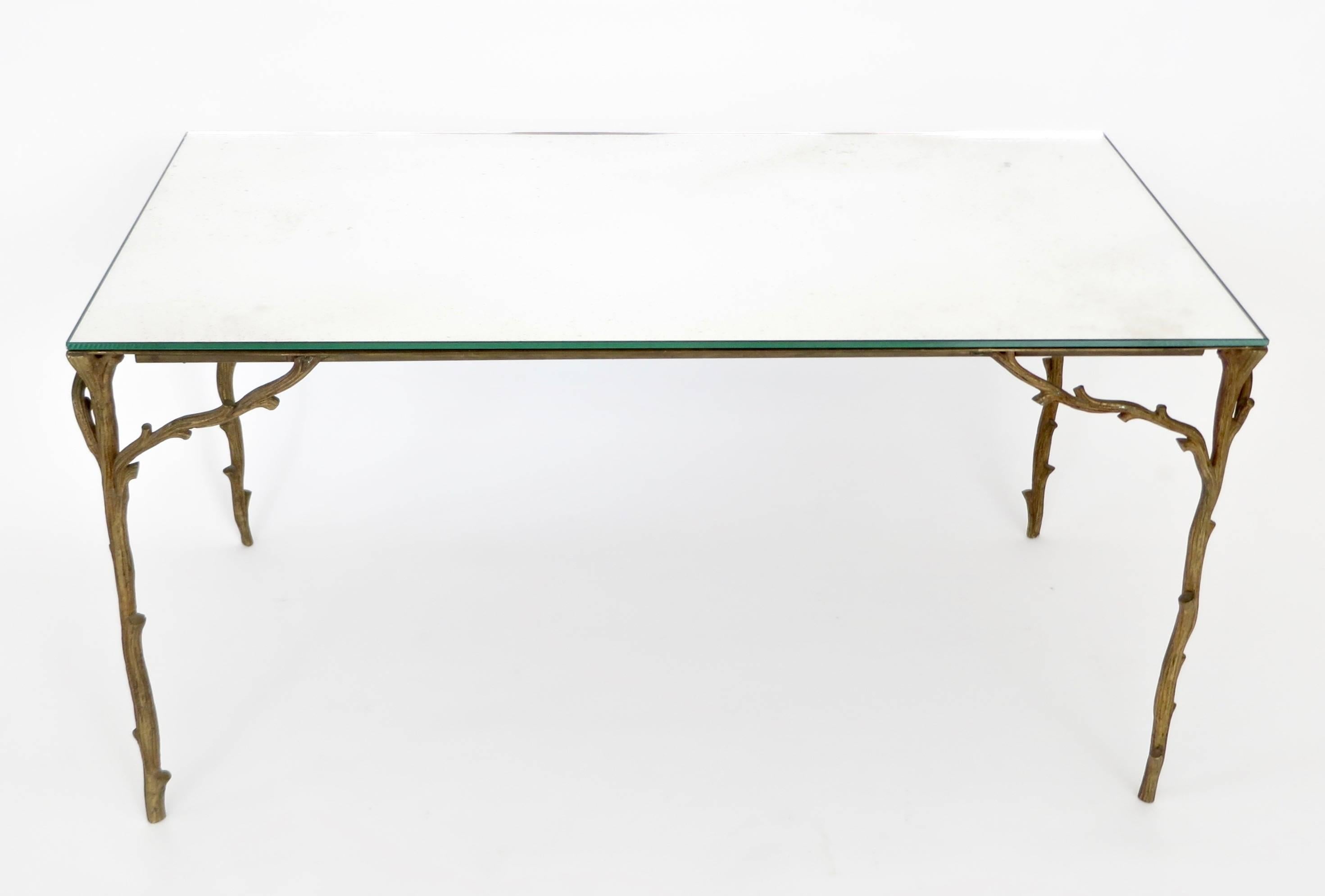 This Maison Bagues bronze based coffee table with very animated bronze legs of branches and not the typical faux bamboo makes it more rare. 
The vegetal and wood shaped design ornament is very organic and lyrical.
The top is a mirrored glass with a