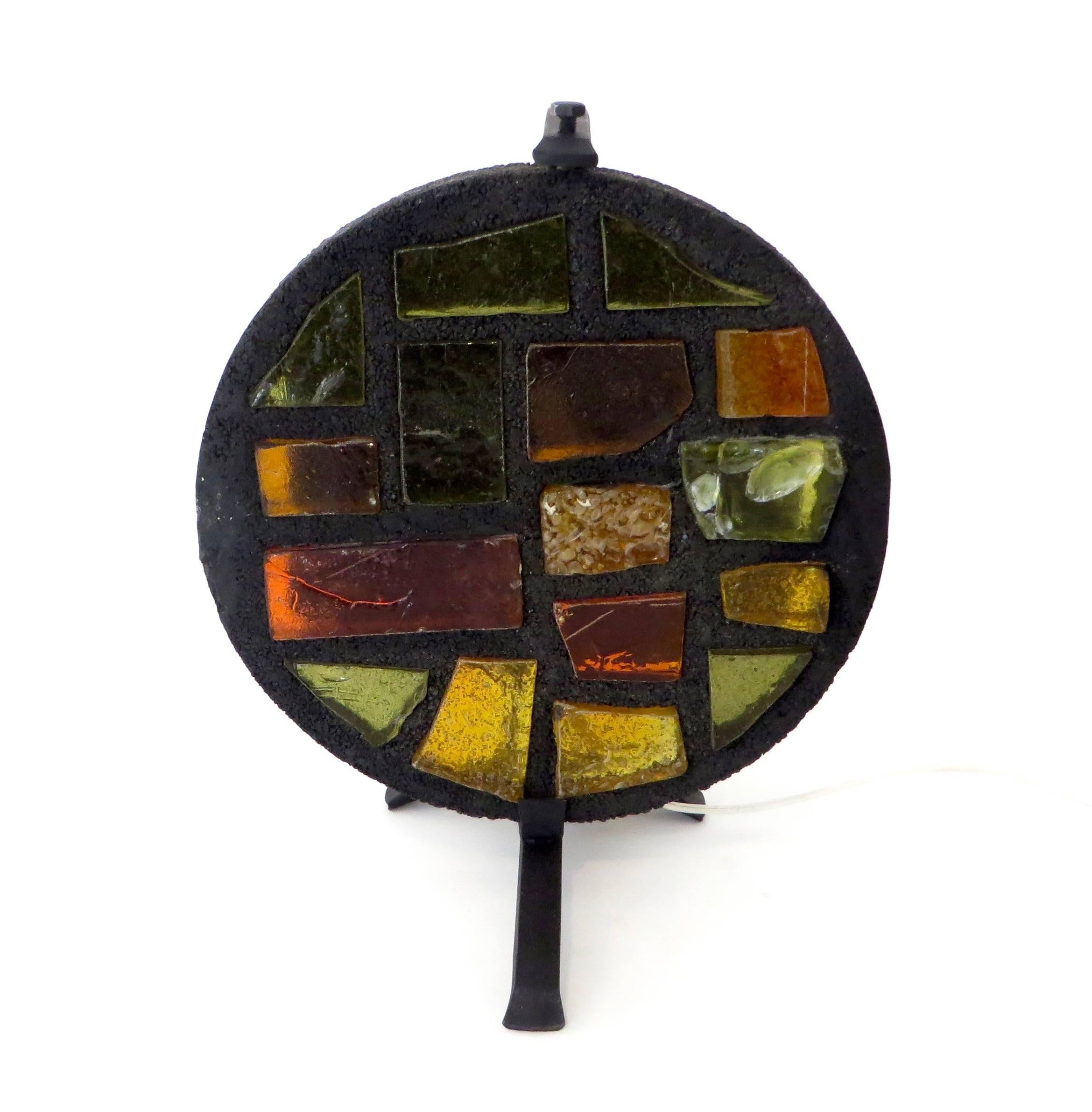 A French multi colored glass mosaic sculptural table lamp by artist Jacques Avoinet. 
The mosaic of colored glass is set in a frame of black stained concrete and on a rotating Brutalist illuminated iron frame. Each piece created by the artist was