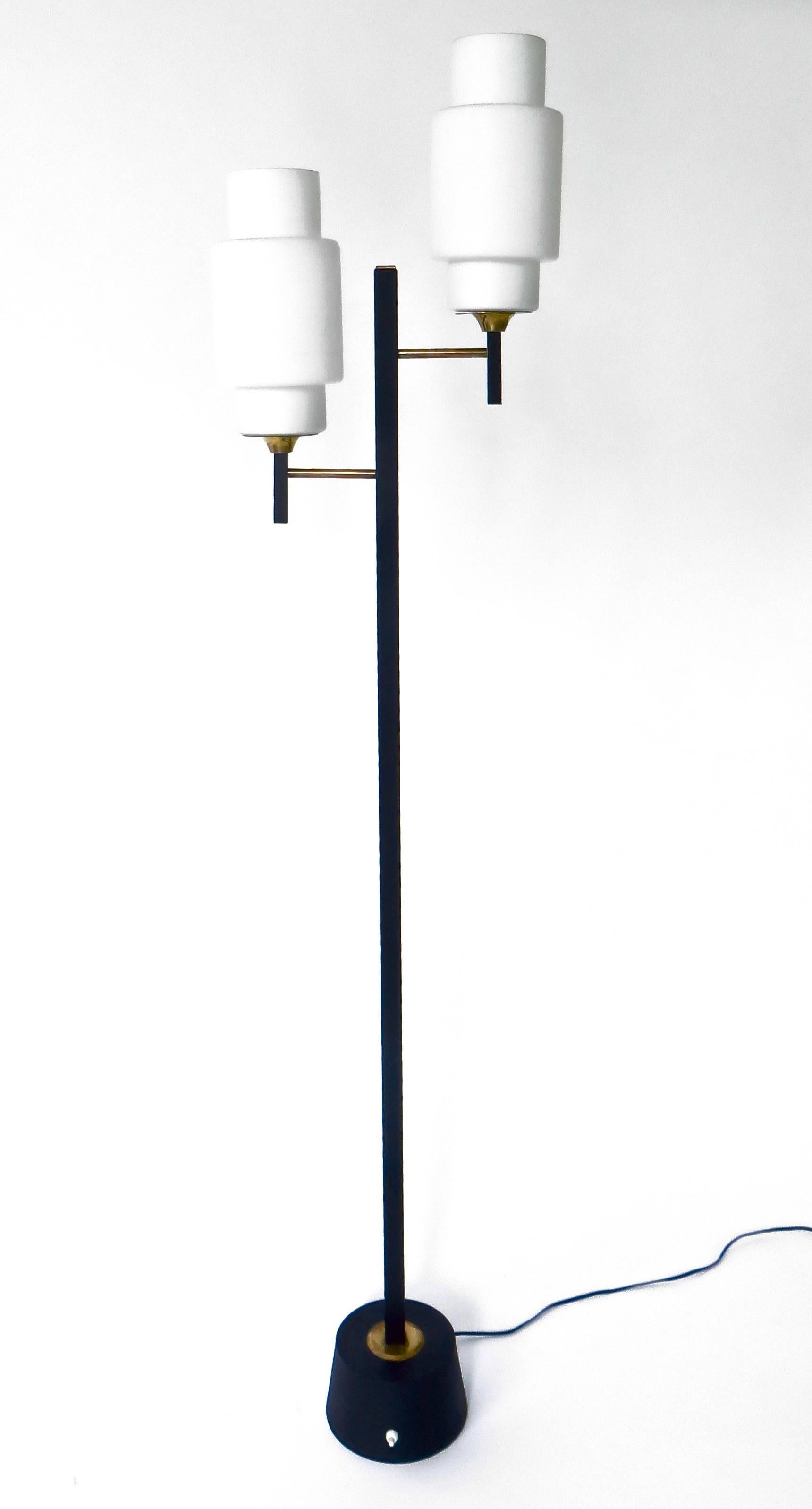 1950s French floor lamp by Maison Lunel with a square section arm resting on a round base decorated with a disc of brass.
On the upper part, two gilt brass rods support two large cylindrical opaline glass shades.
The lamp terminates on a very