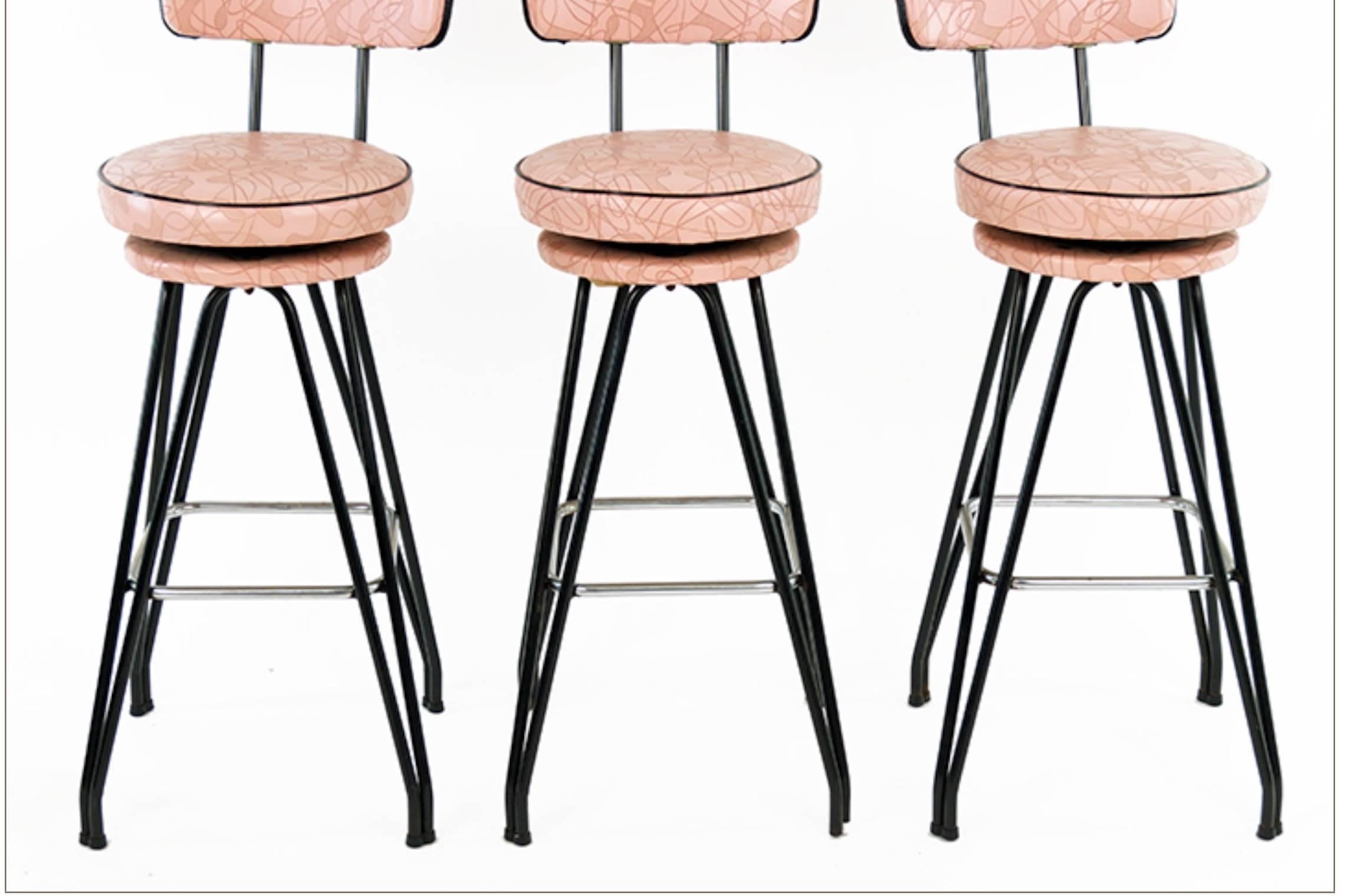 Set of three Kitch Mid-Century bar stools with pink upholstery, black piping.